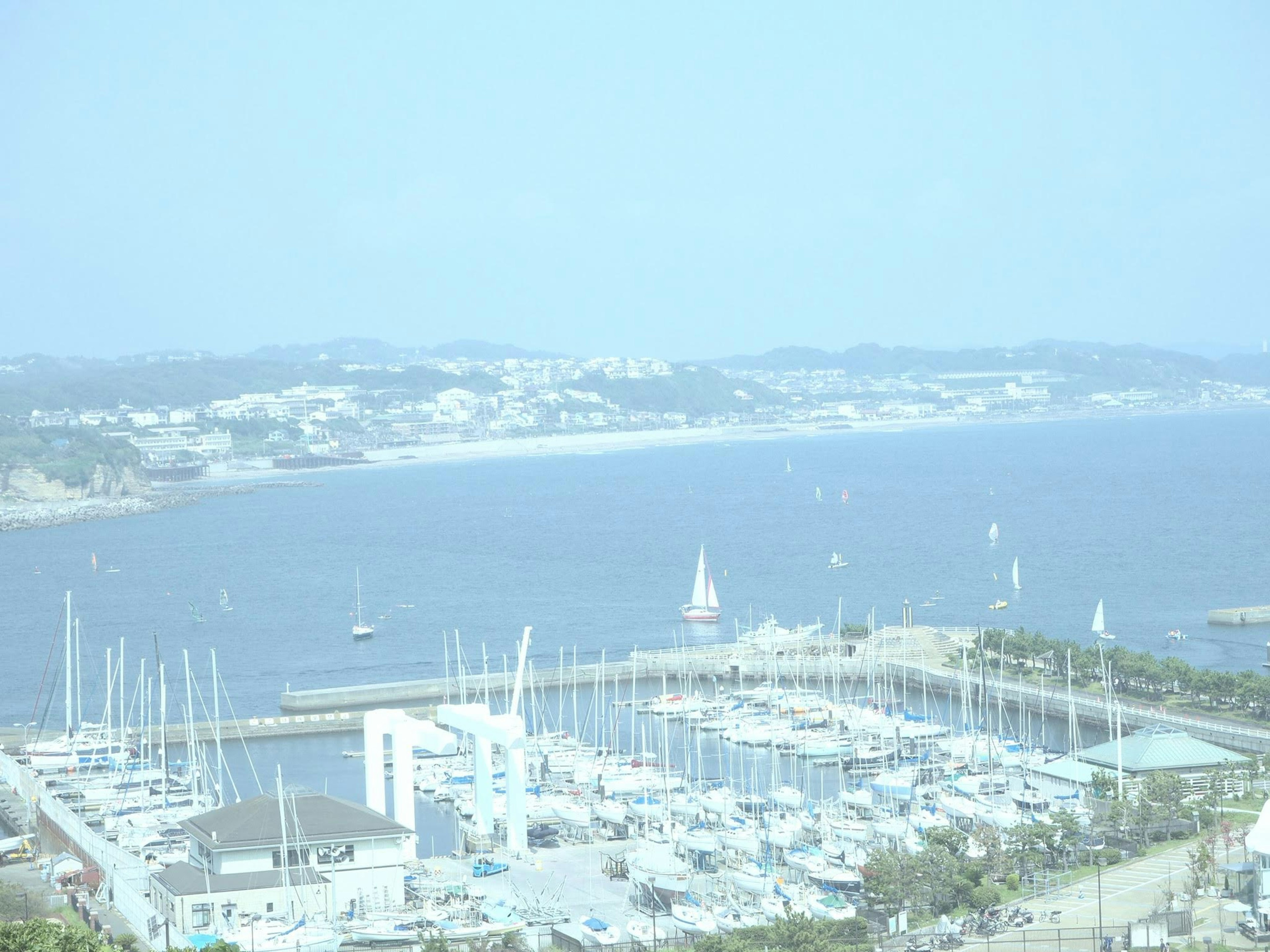 Pemandangan pantai dengan marina dan perahu layar di kejauhan