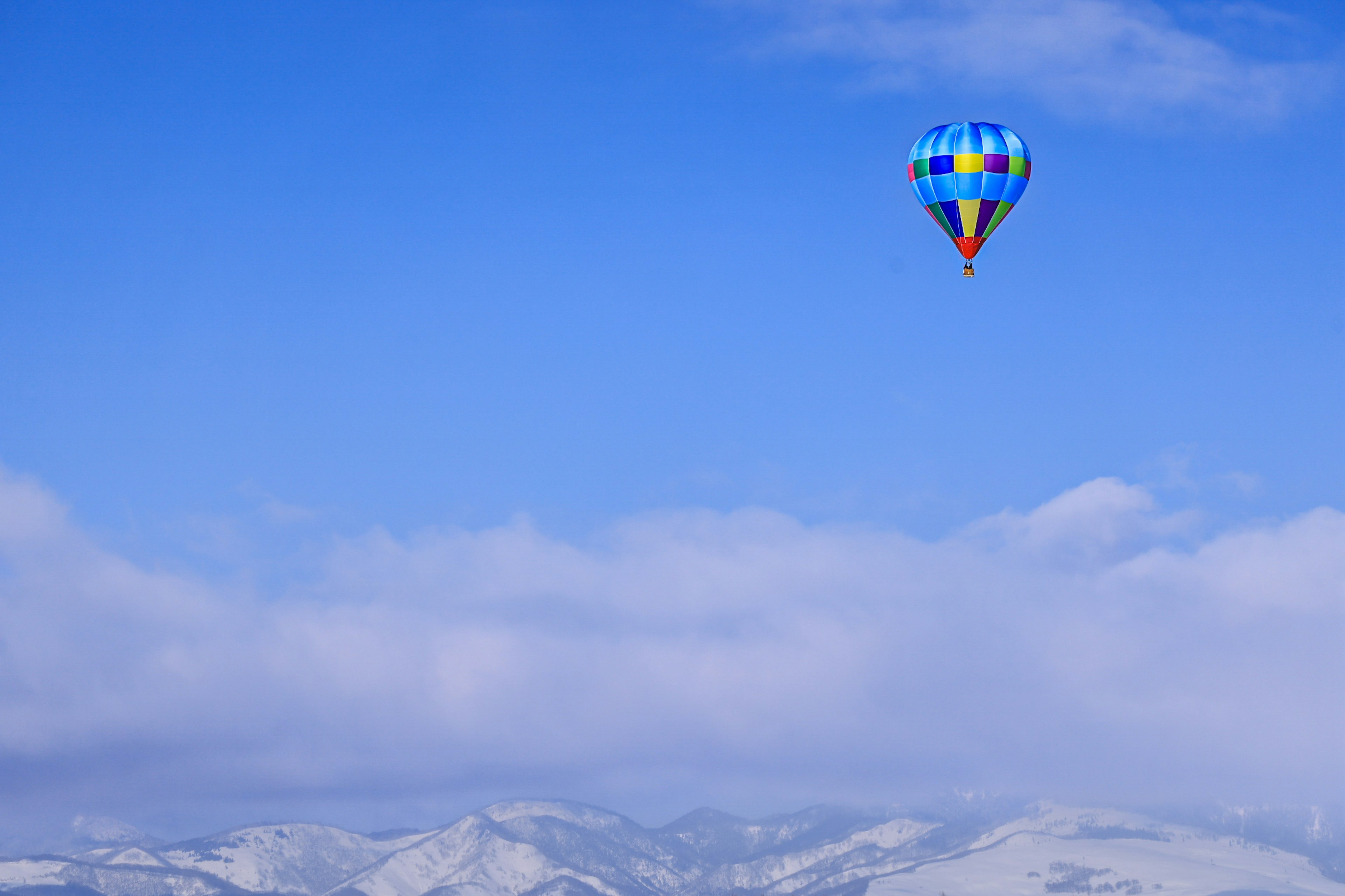 Globo aerostático colorido volando en un cielo azul con montañas nevadas