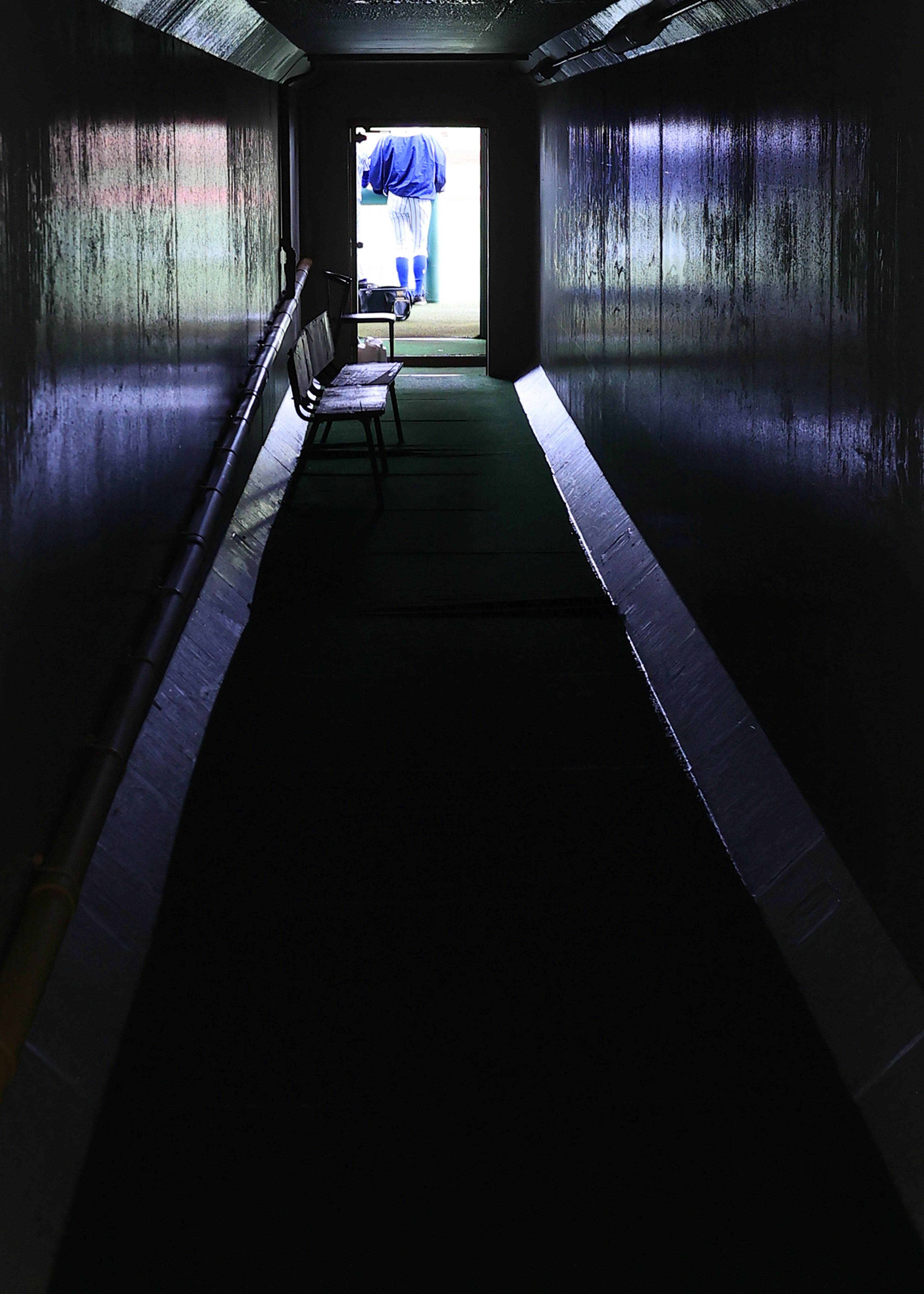 A dimly lit corridor leading to a bright door with a chair visible