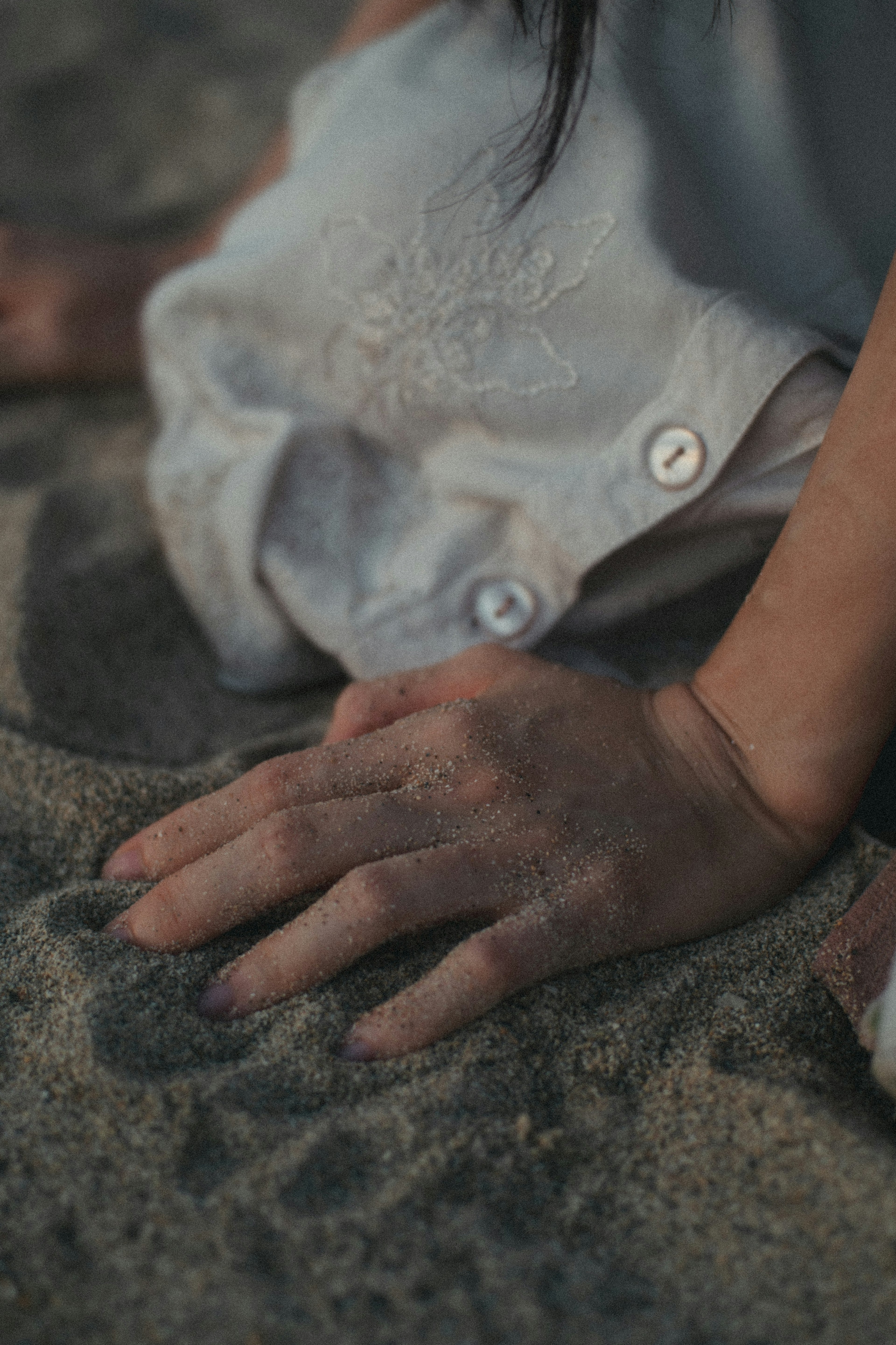 Child's hand touching the sand with a white shirt and buttons