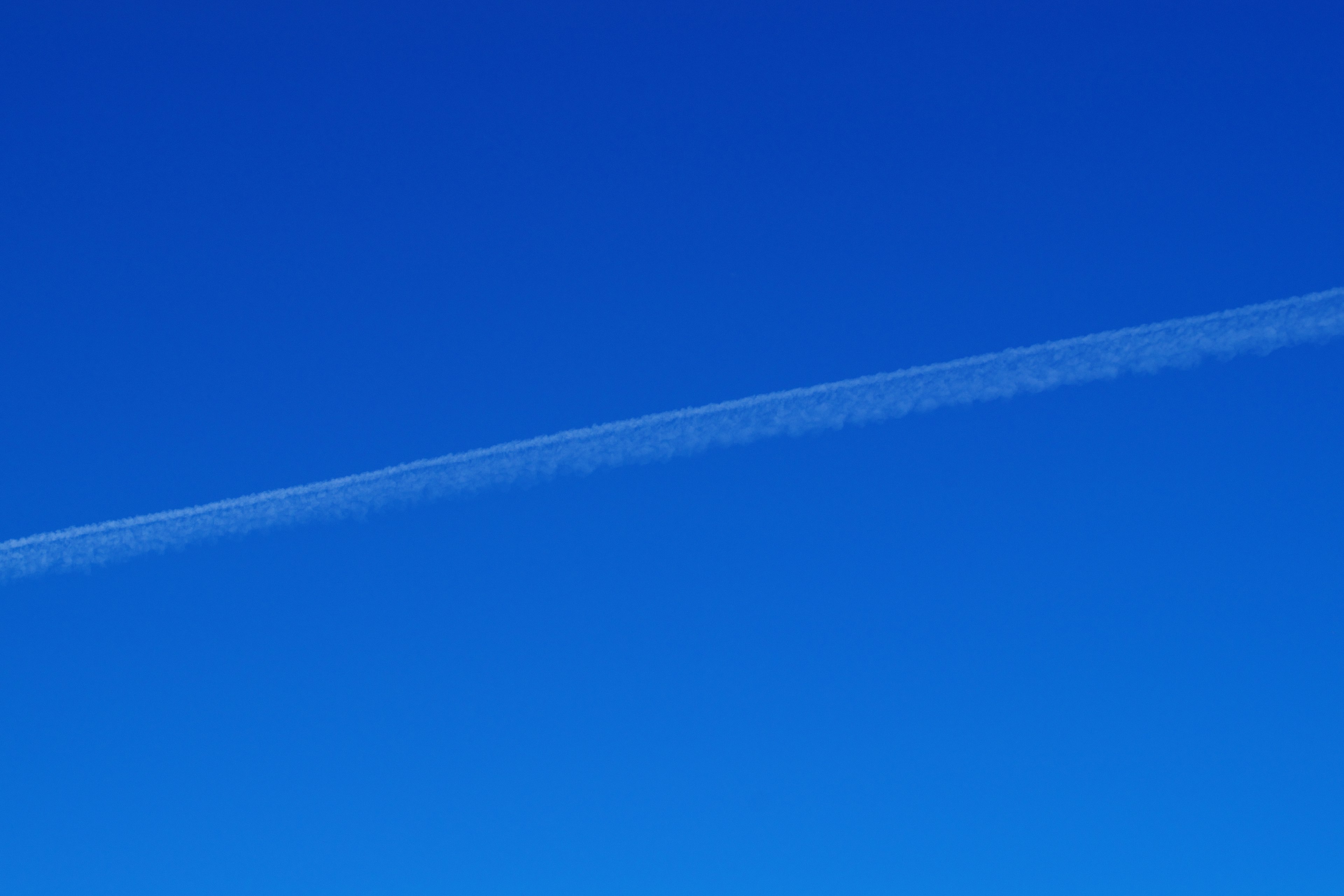 A clear blue sky with a white contrail stretching across