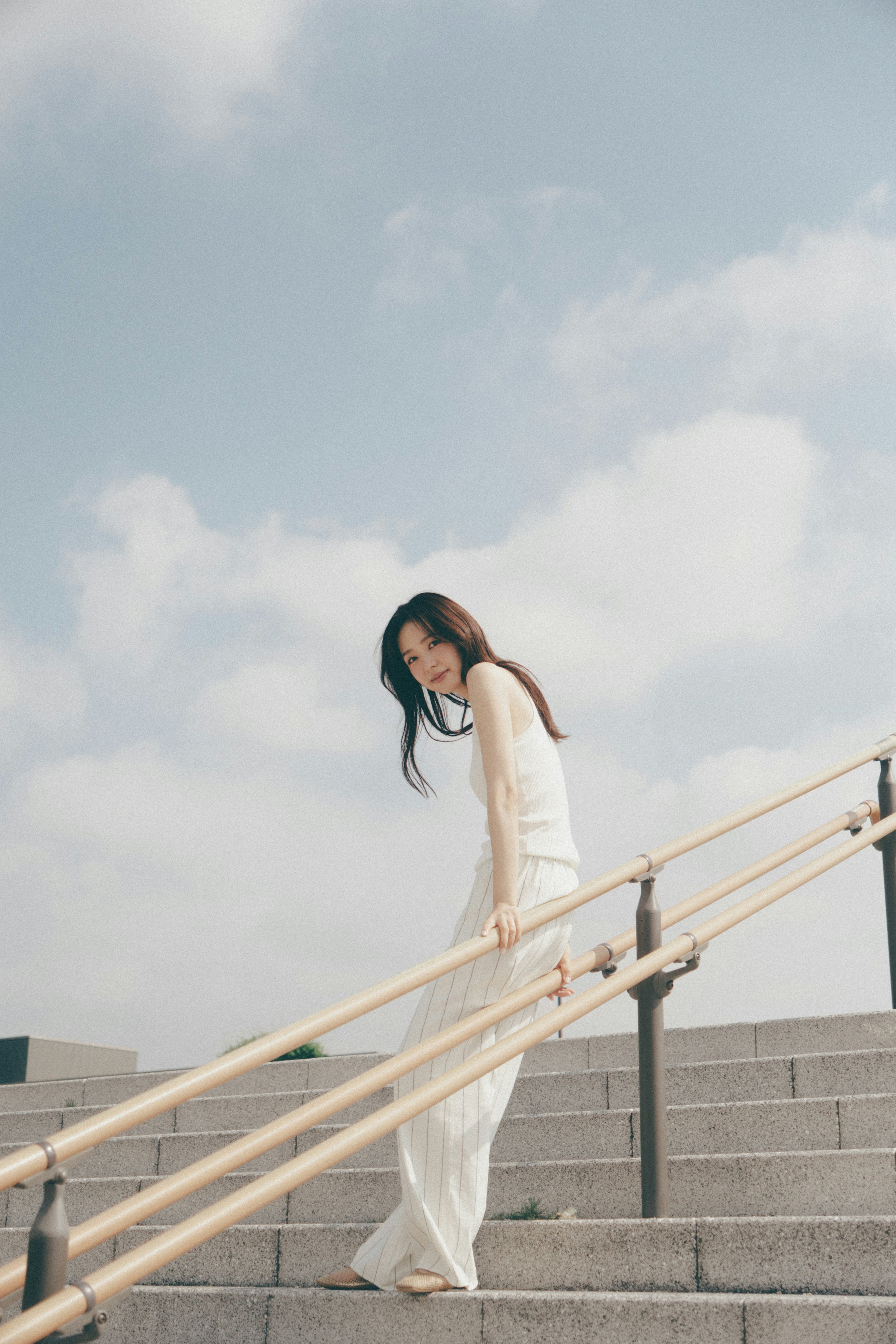 A woman in a white dress descending stairs under a blue sky