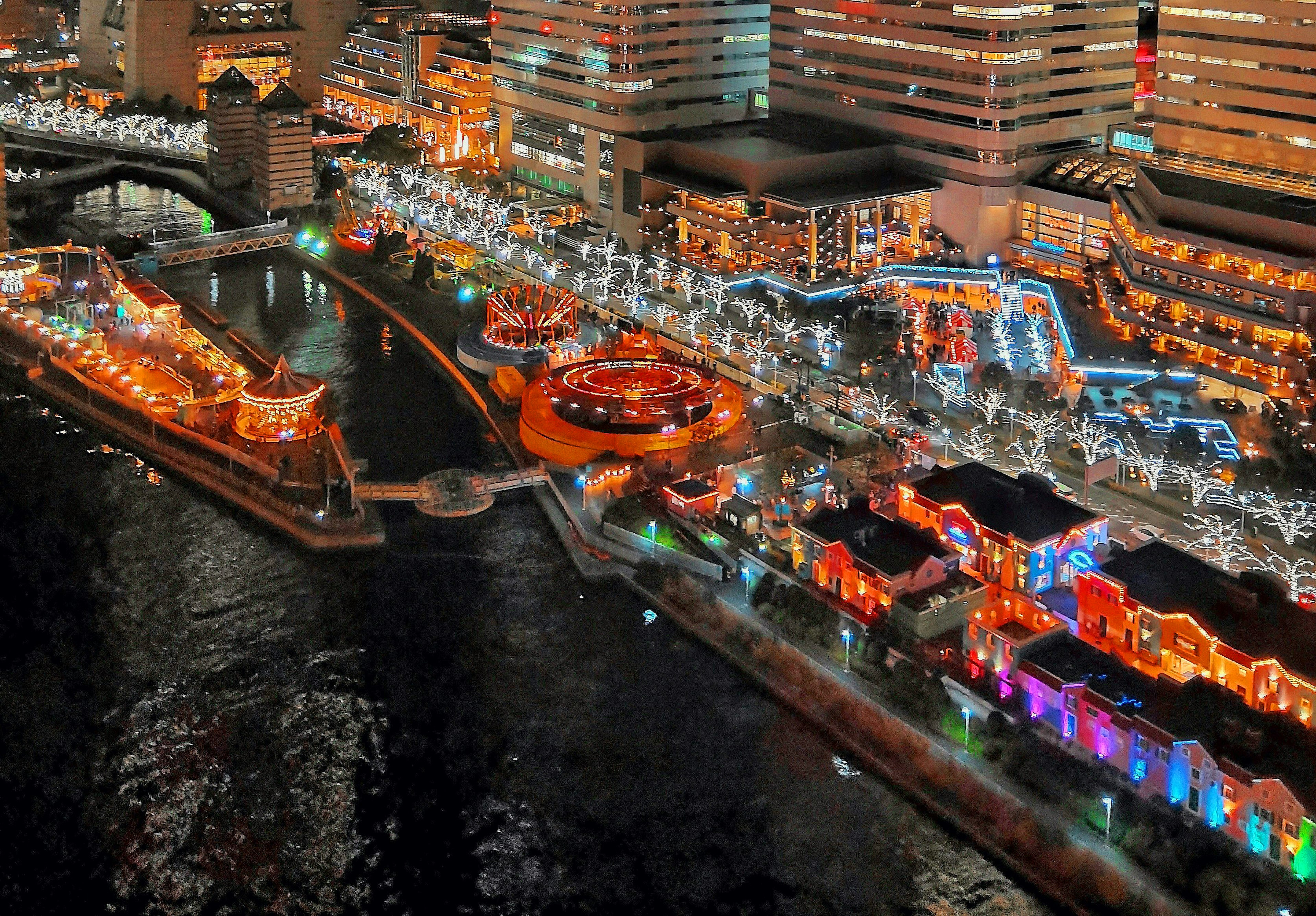 Nachtansicht eines Freizeitparks am Fluss mit bunten Lichtern