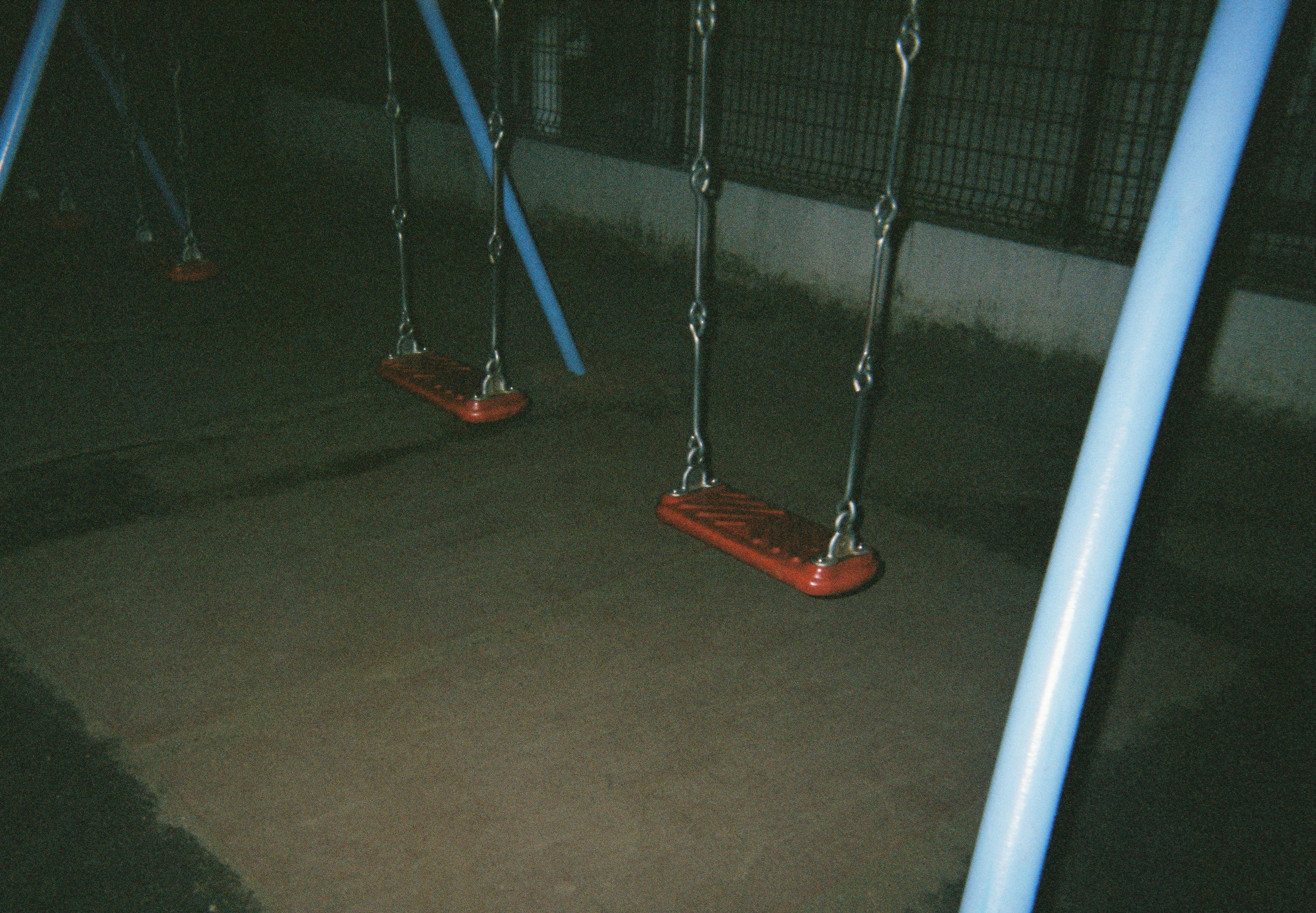 Swings in a dark park with red seats and blue frames