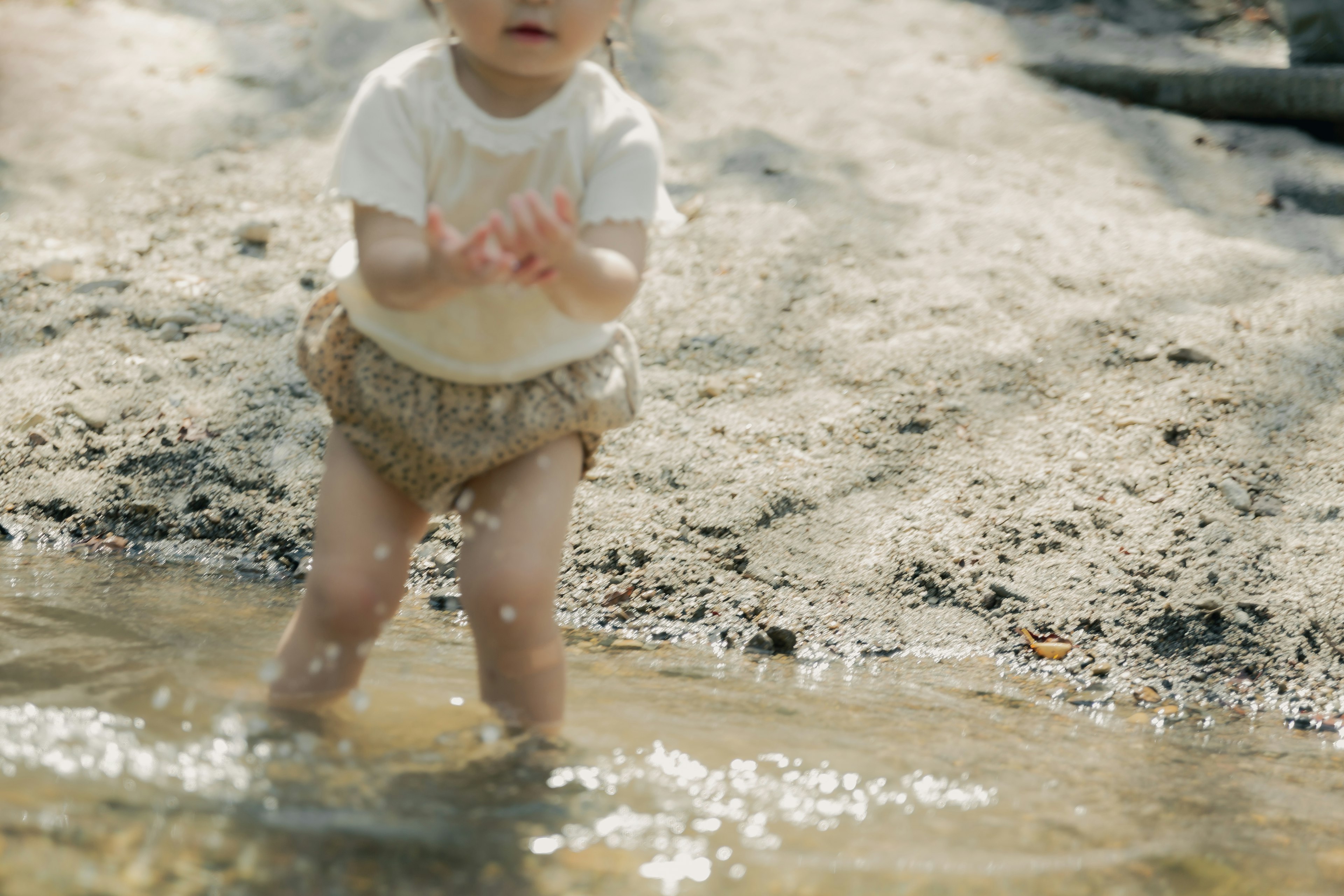 Child playing in a puddle wearing beige shorts and a white t-shirt