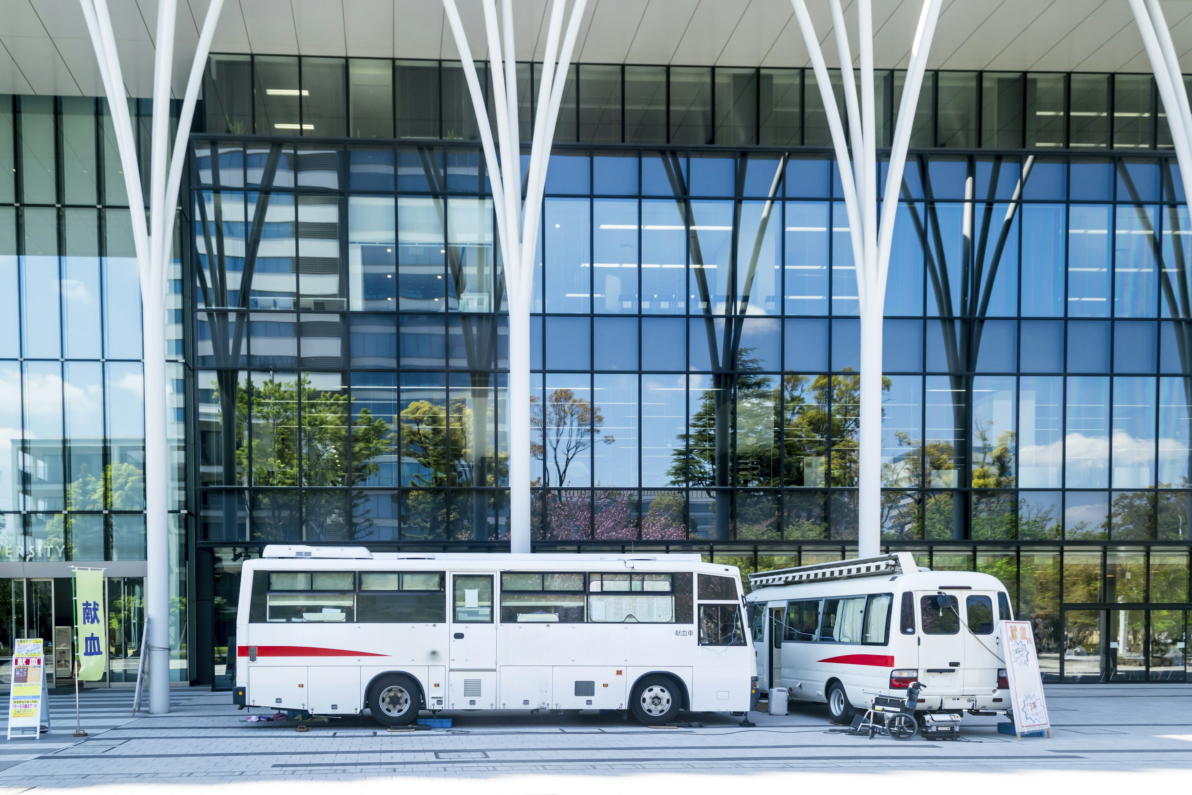 Autobus et van blancs garés devant un bâtiment moderne en verre