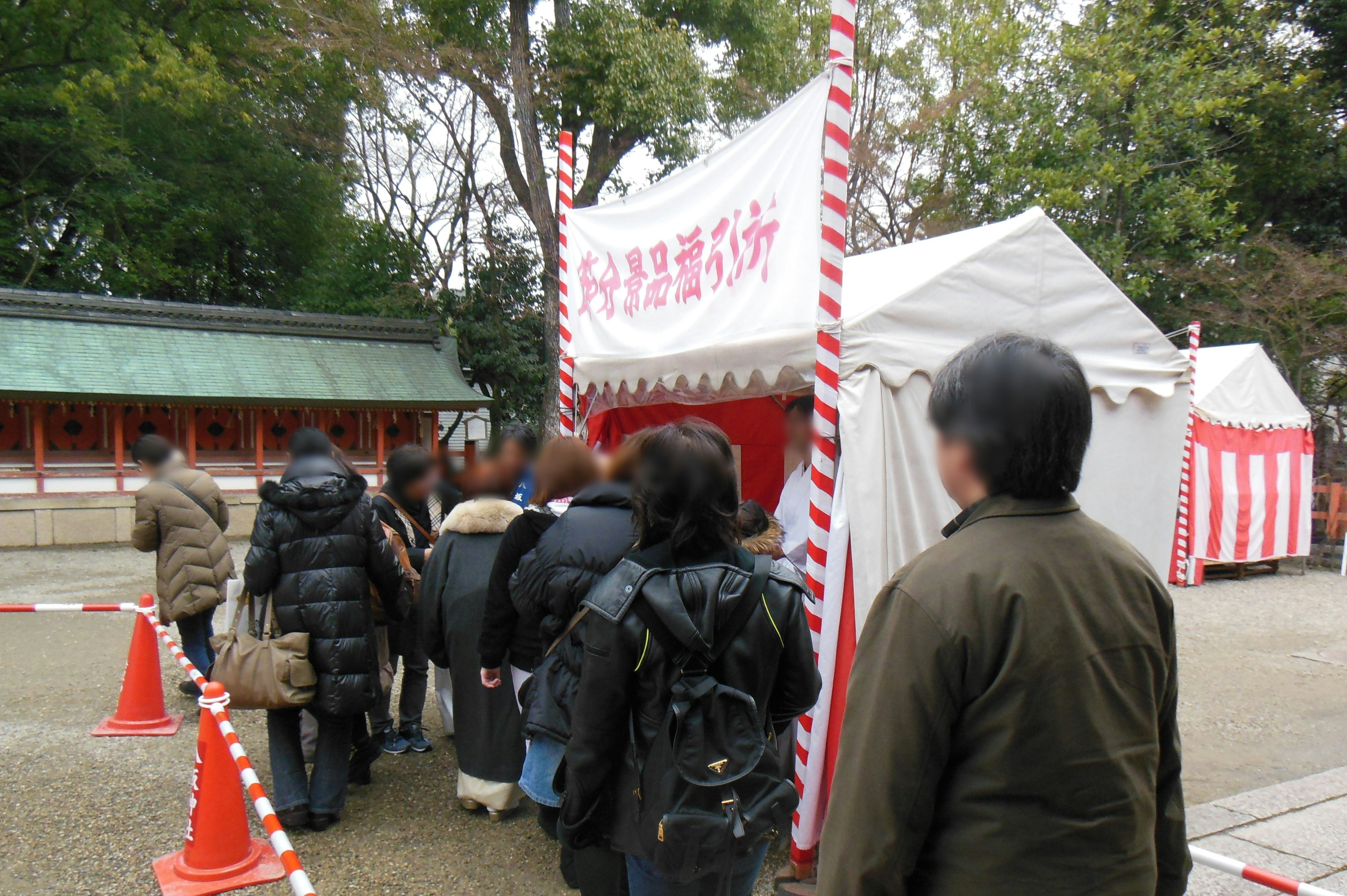 在紅白帳篷前排隊的人們，背景是神社