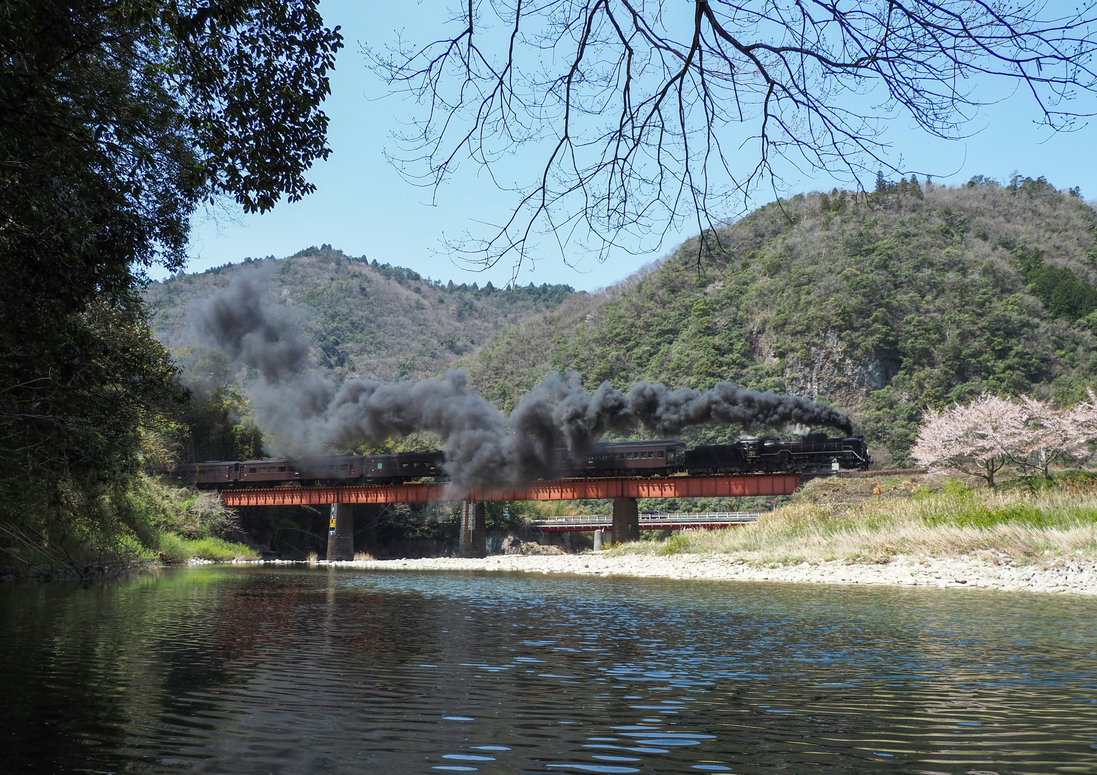 川の上を走る蒸気機関車と山々の風景