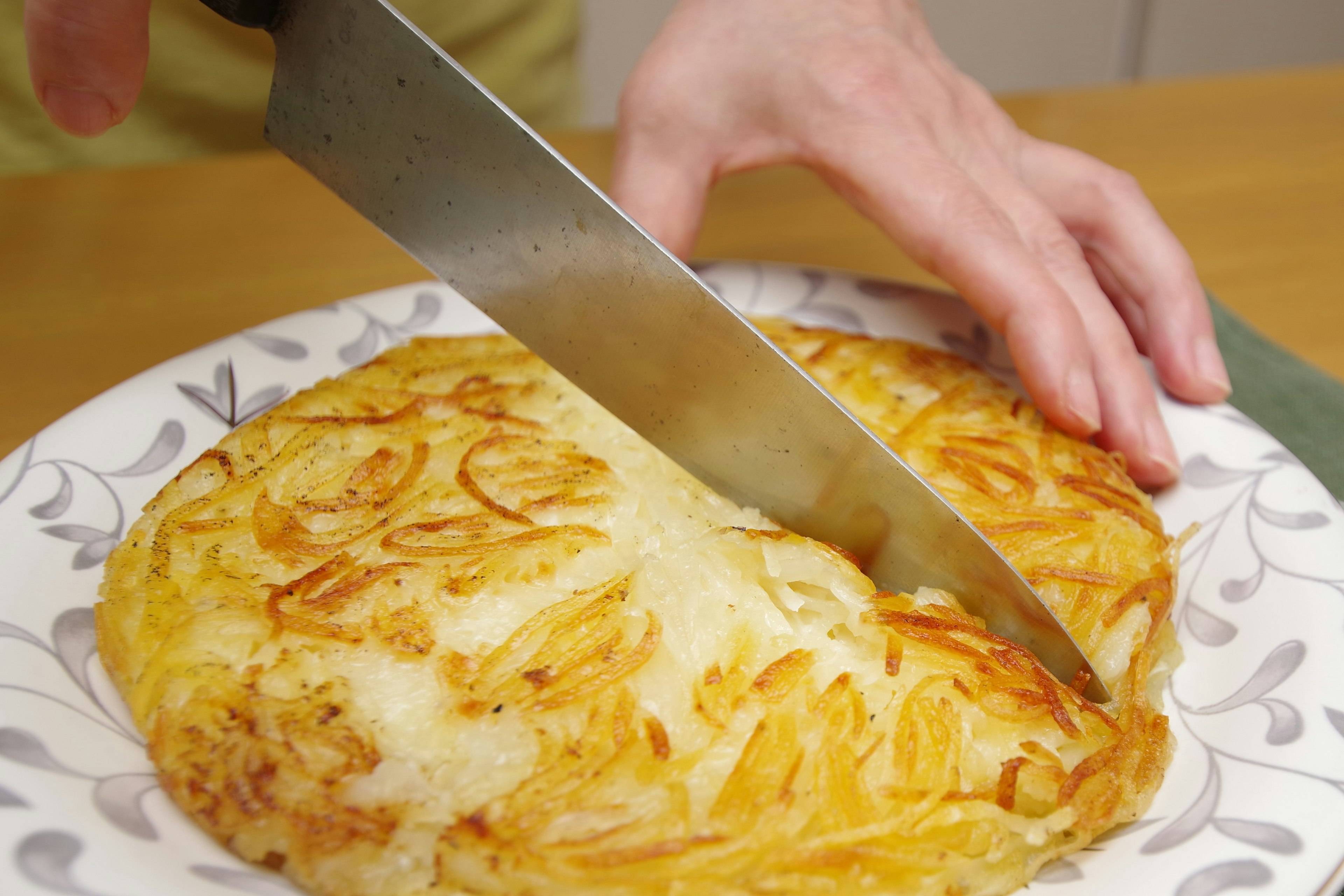 Una mano cortando una tortilla en un plato decorativo