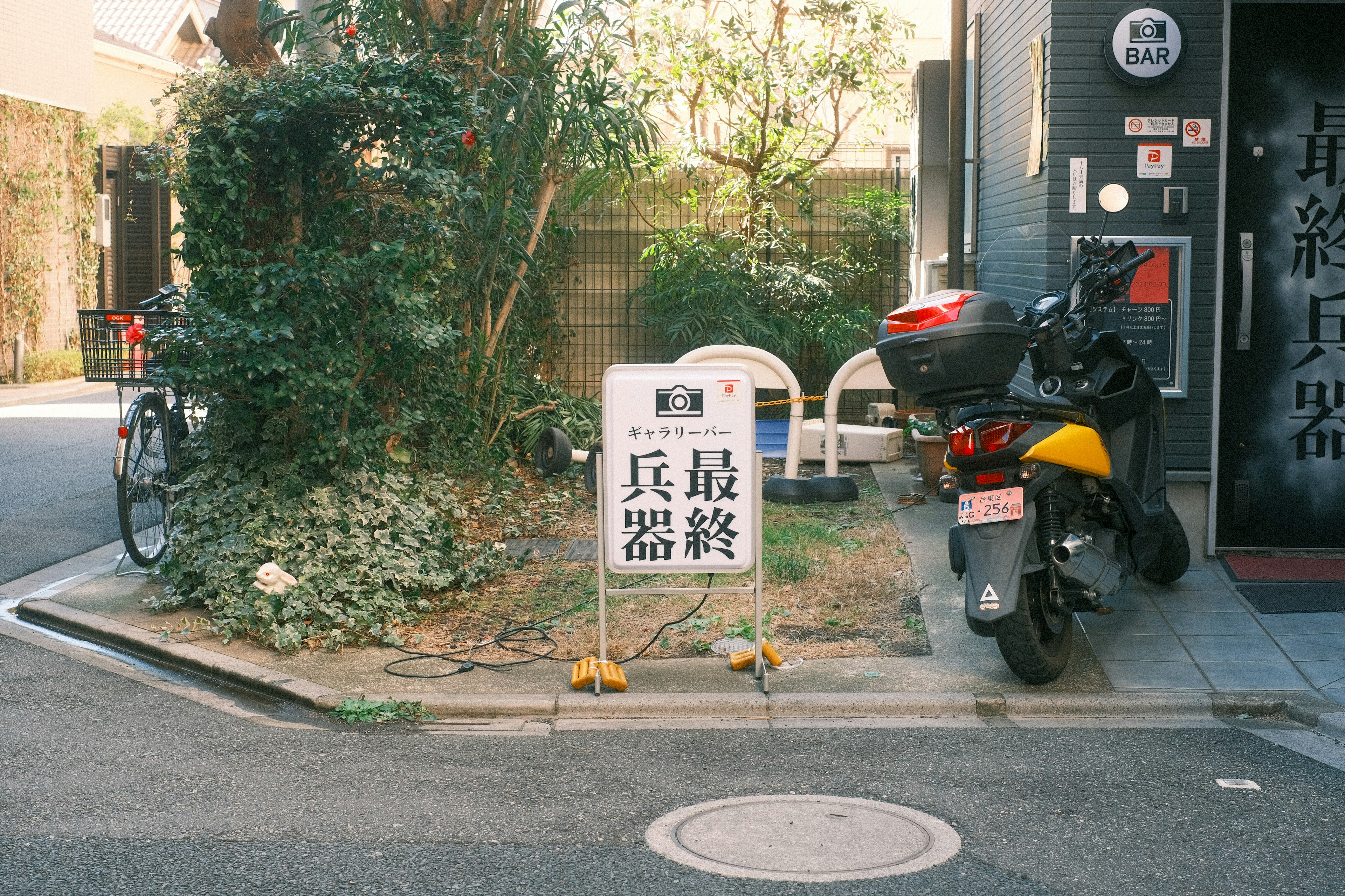 角にある自転車とバイクの近くに立つ看板と緑の植物