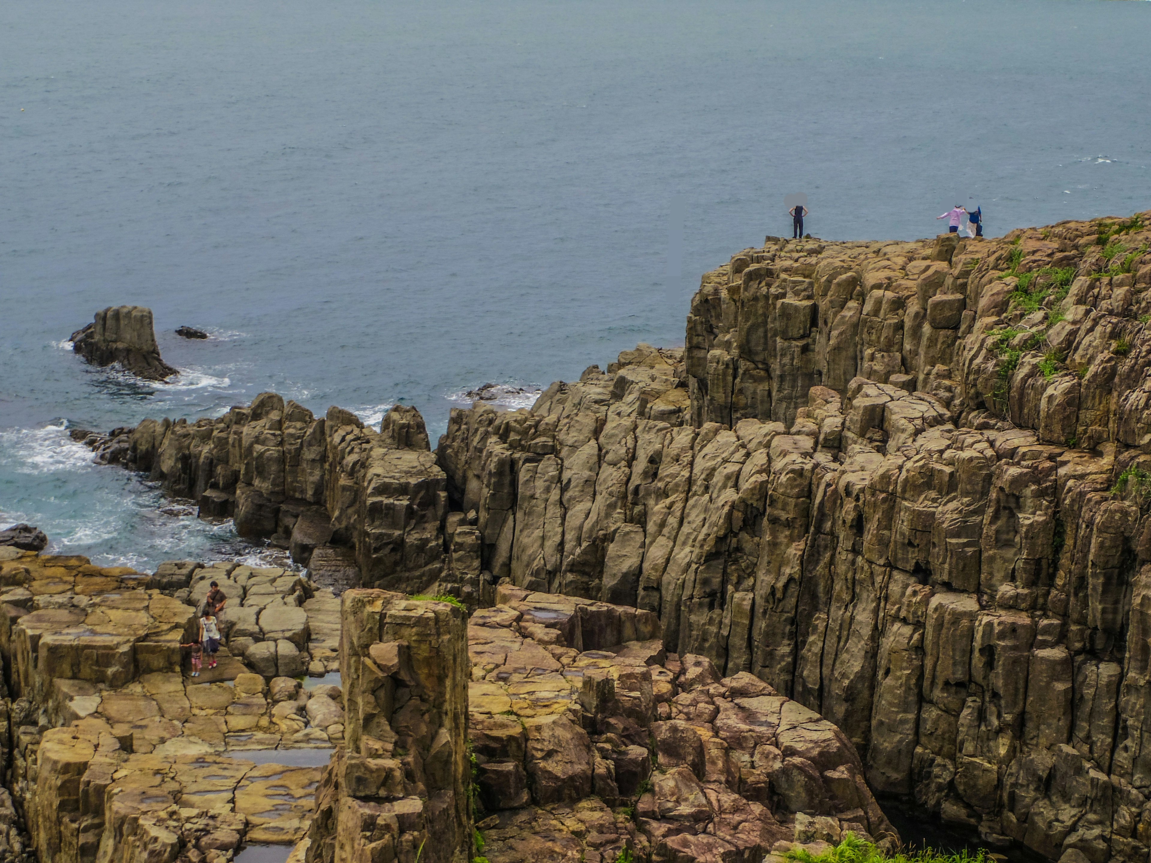 Personnes debout sur une côte rocheuse surplombant une mer calme