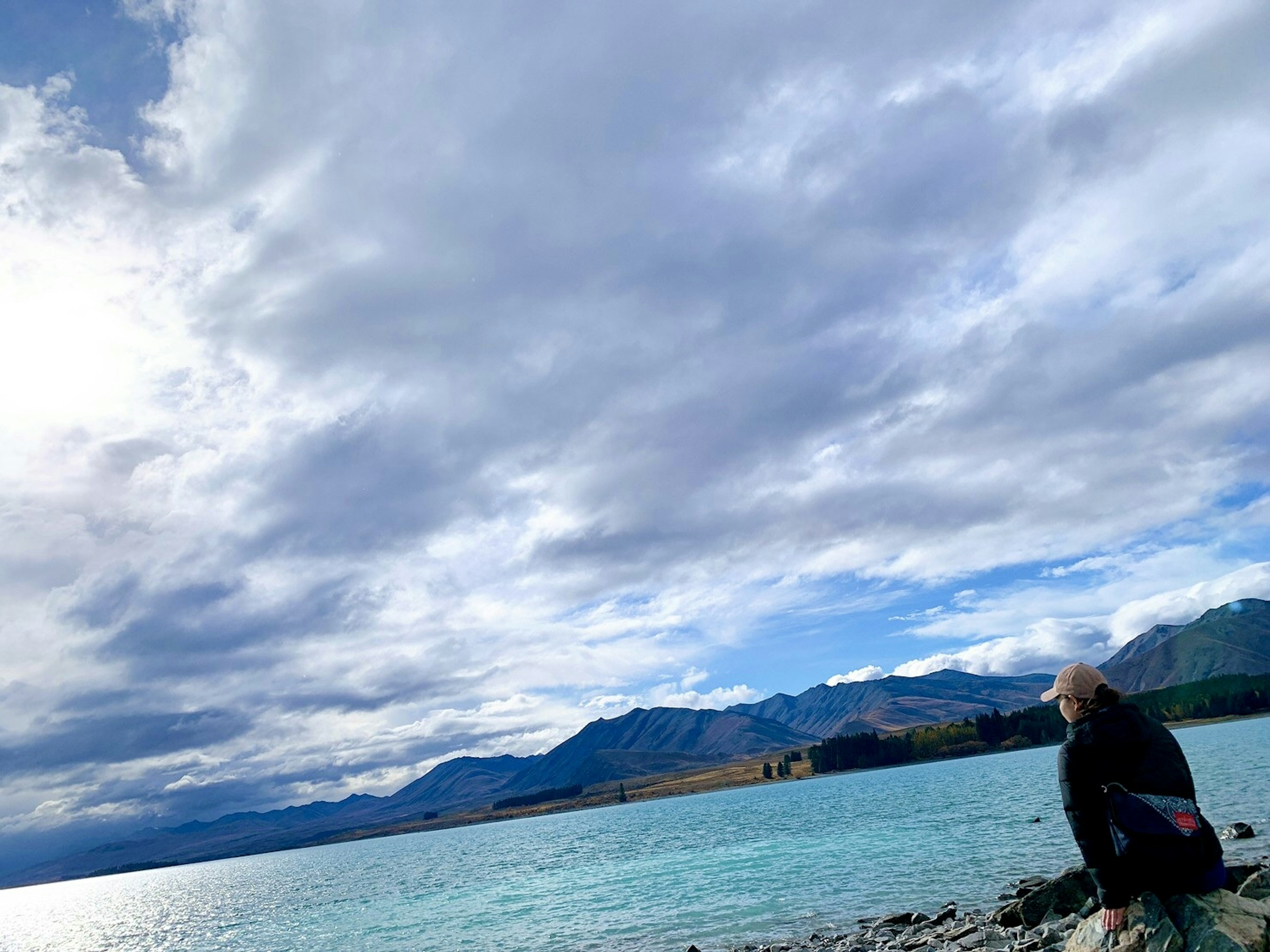 青い湖のほとりで座る人物と美しい山々の風景