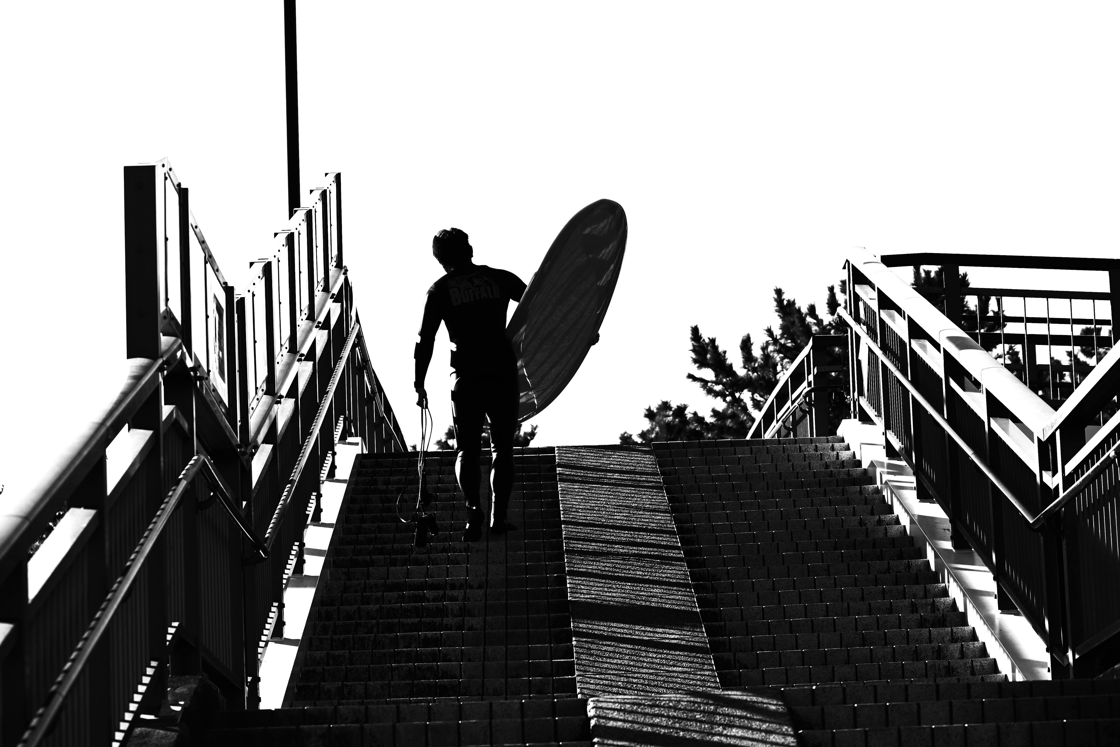 Silhouette einer Person, die ein Surfbrett trägt und eine Treppe hinaufgeht