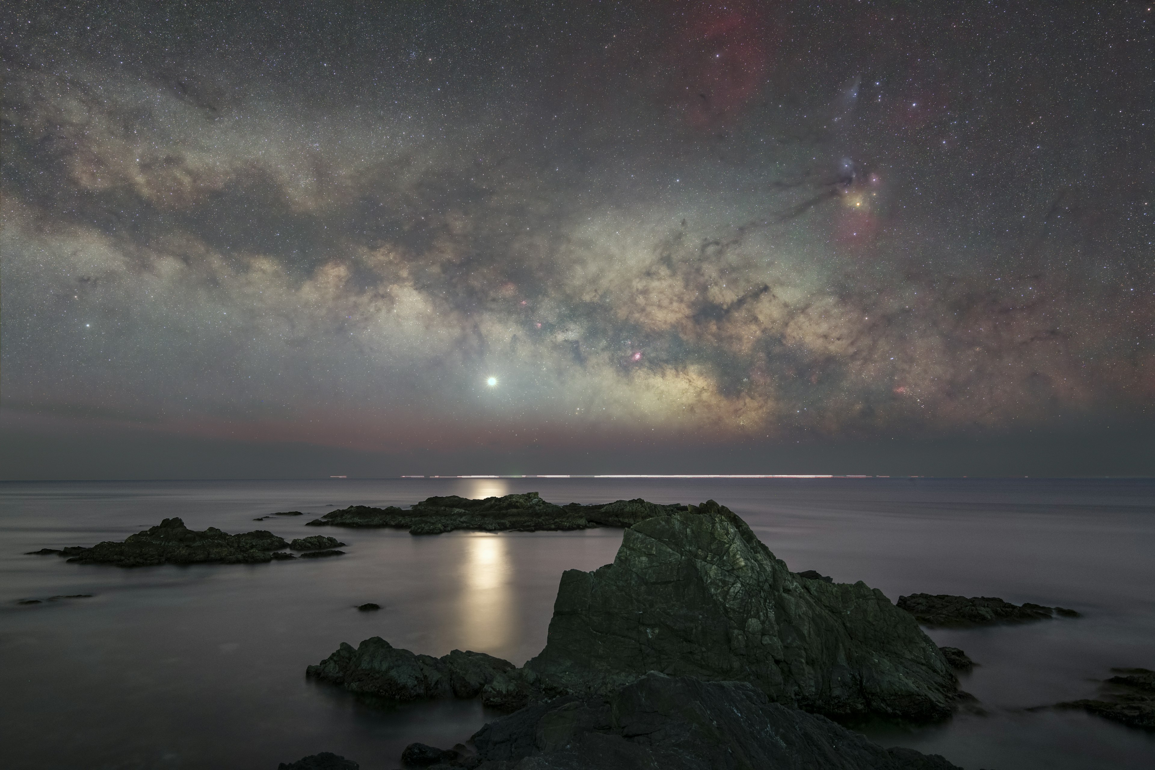 Ciel étoilé au-dessus d'une mer calme avec des rochers visibles