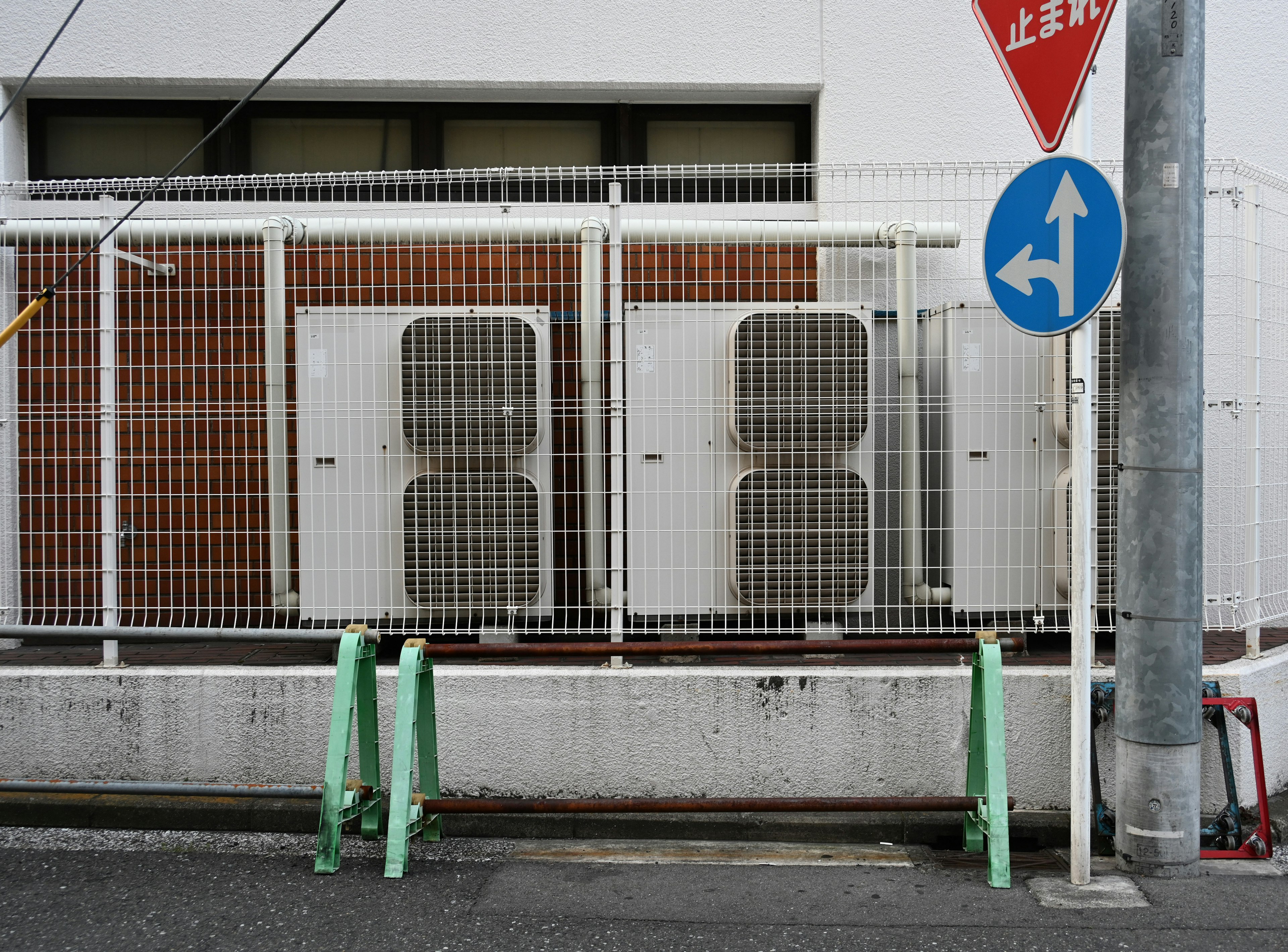 Two air conditioning units behind a white fence with a blue directional traffic sign