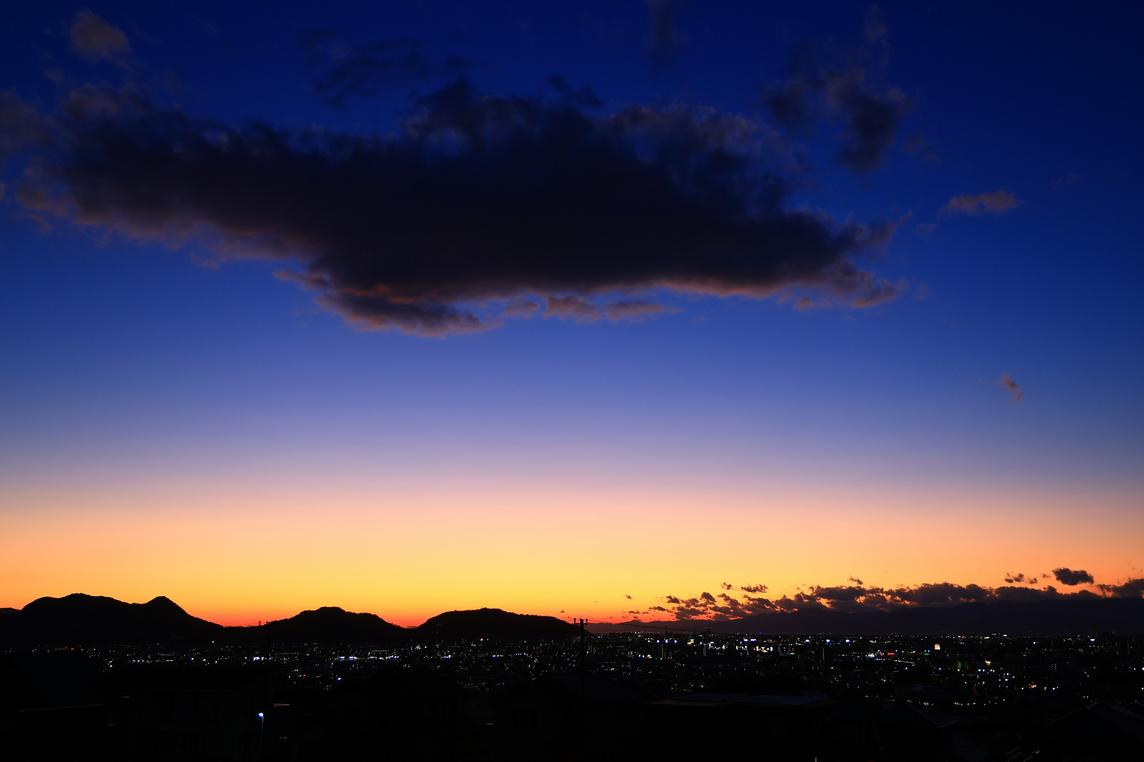 Silhouette of mountains against a sunset sky with a single cloud