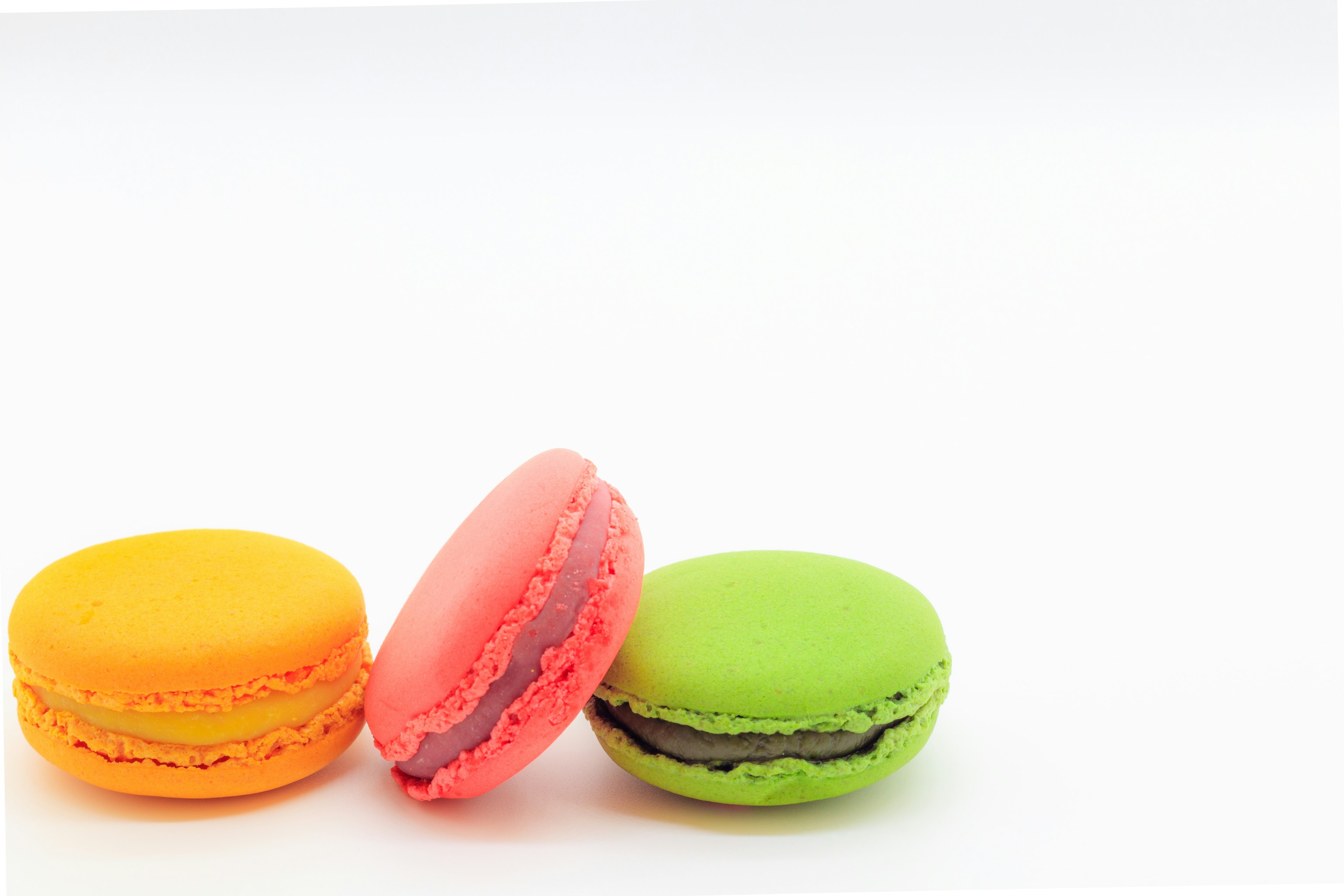 Colorful macarons in orange, pink, and green on a white background