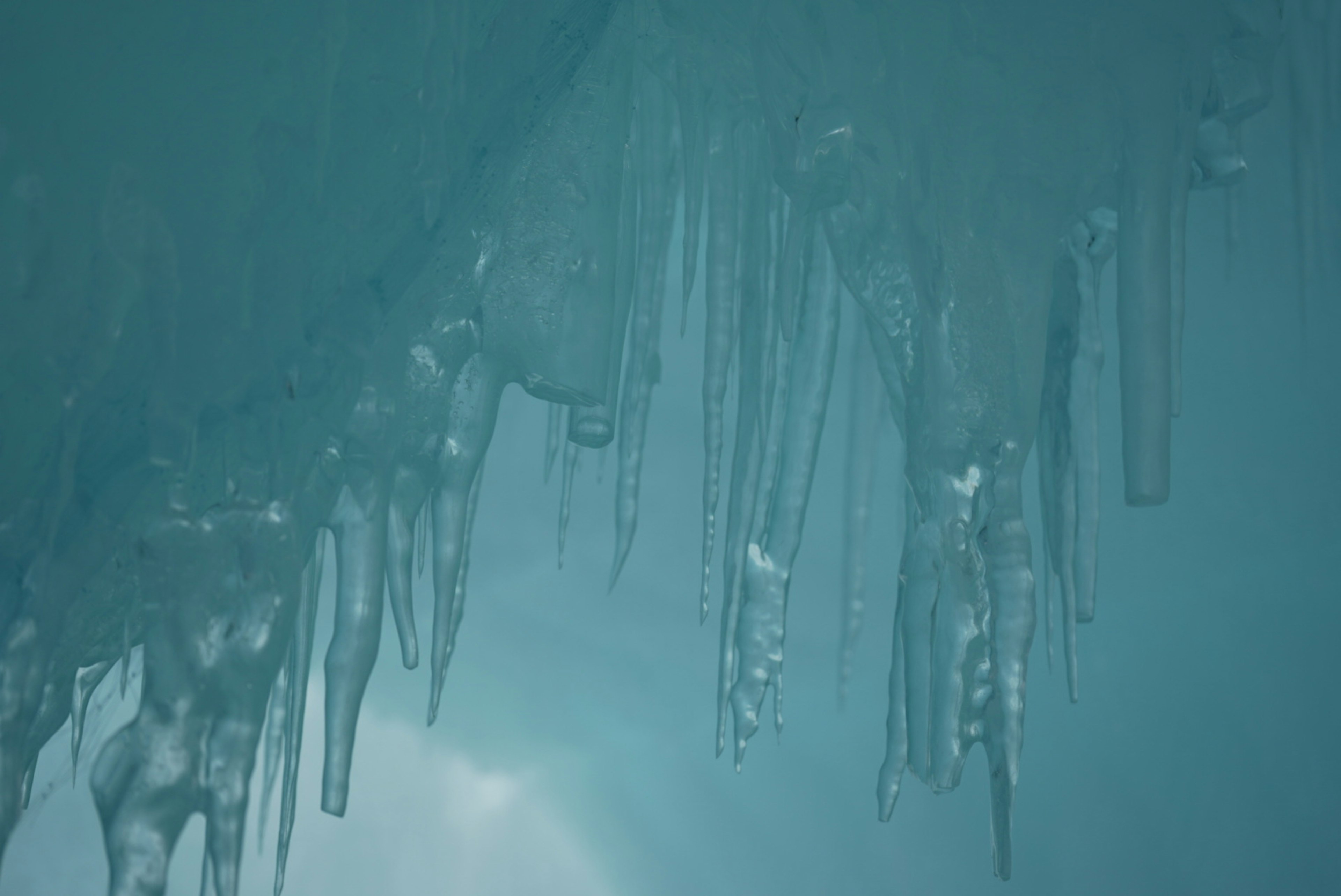 Nahaufnahme von Eiszapfen, die unter einer blauen Eisoberfläche hängen