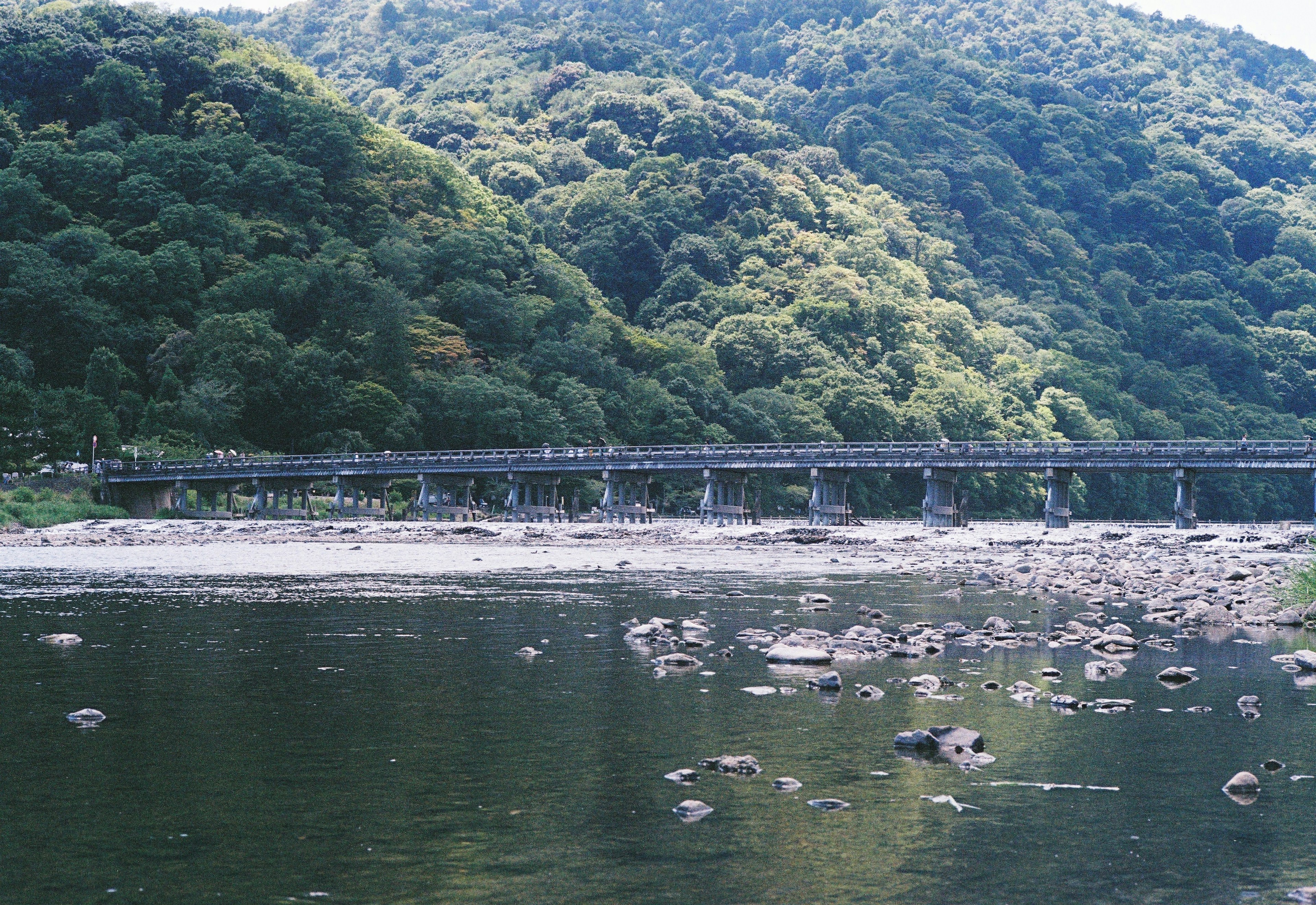 Wooden bridge spanning a tranquil river surrounded by lush green mountains