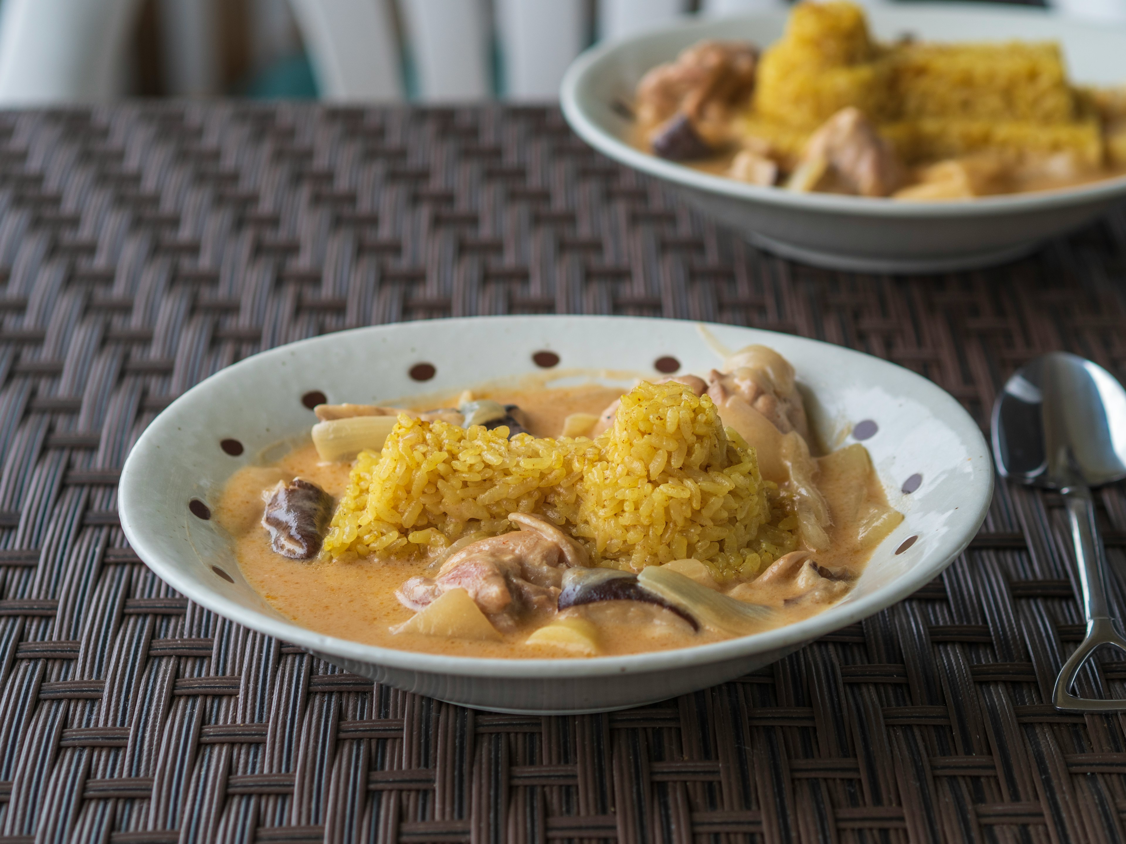 Piring nasi kuning dengan saus krim dan ayam disajikan di atas meja anyaman