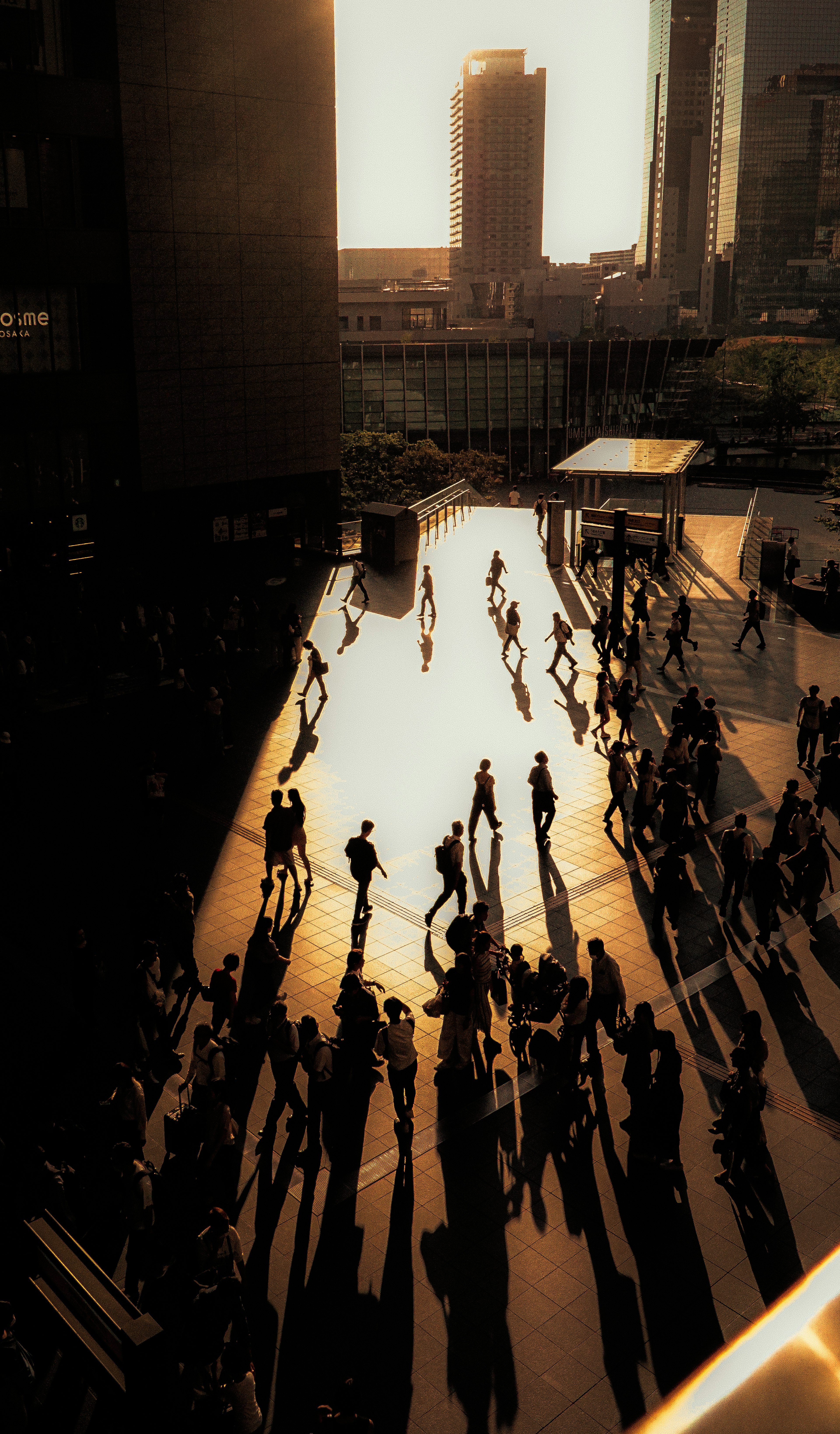 Silhouetten von Menschen, die in einem Stadtplatz mit Sonnenuntergang im Hintergrund gehen