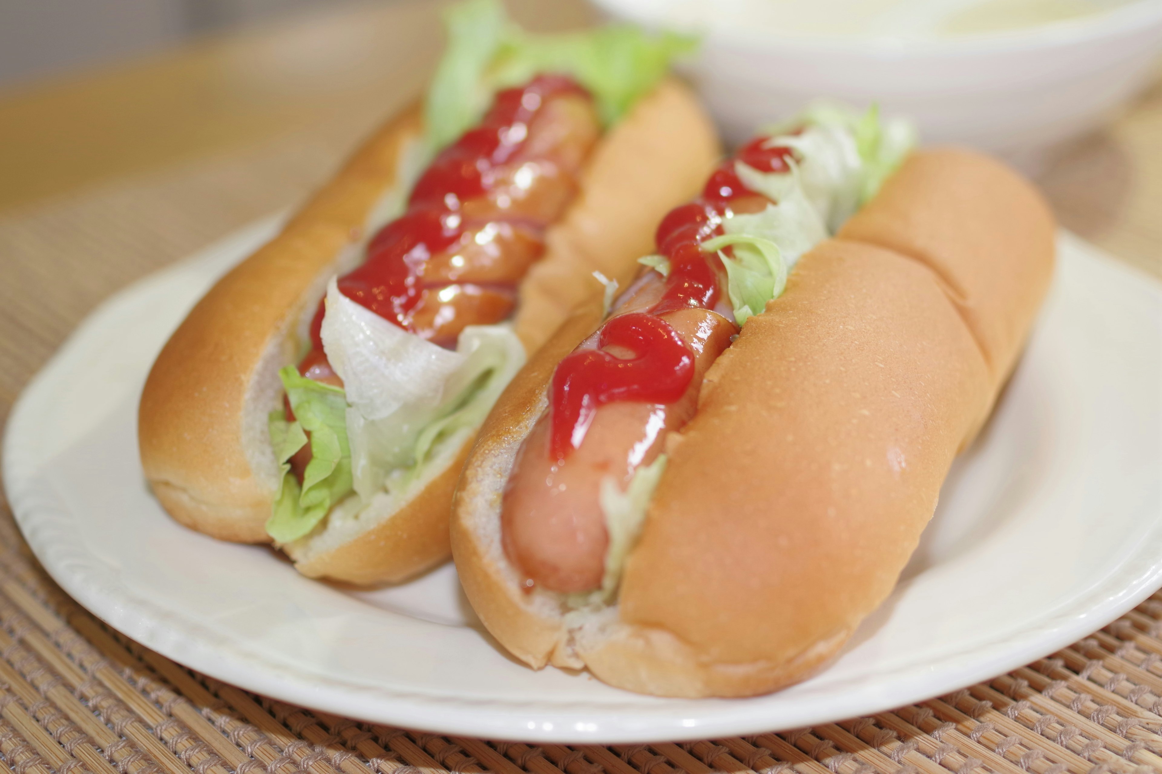 Two hot dogs served on a plate with lettuce and ketchup toppings