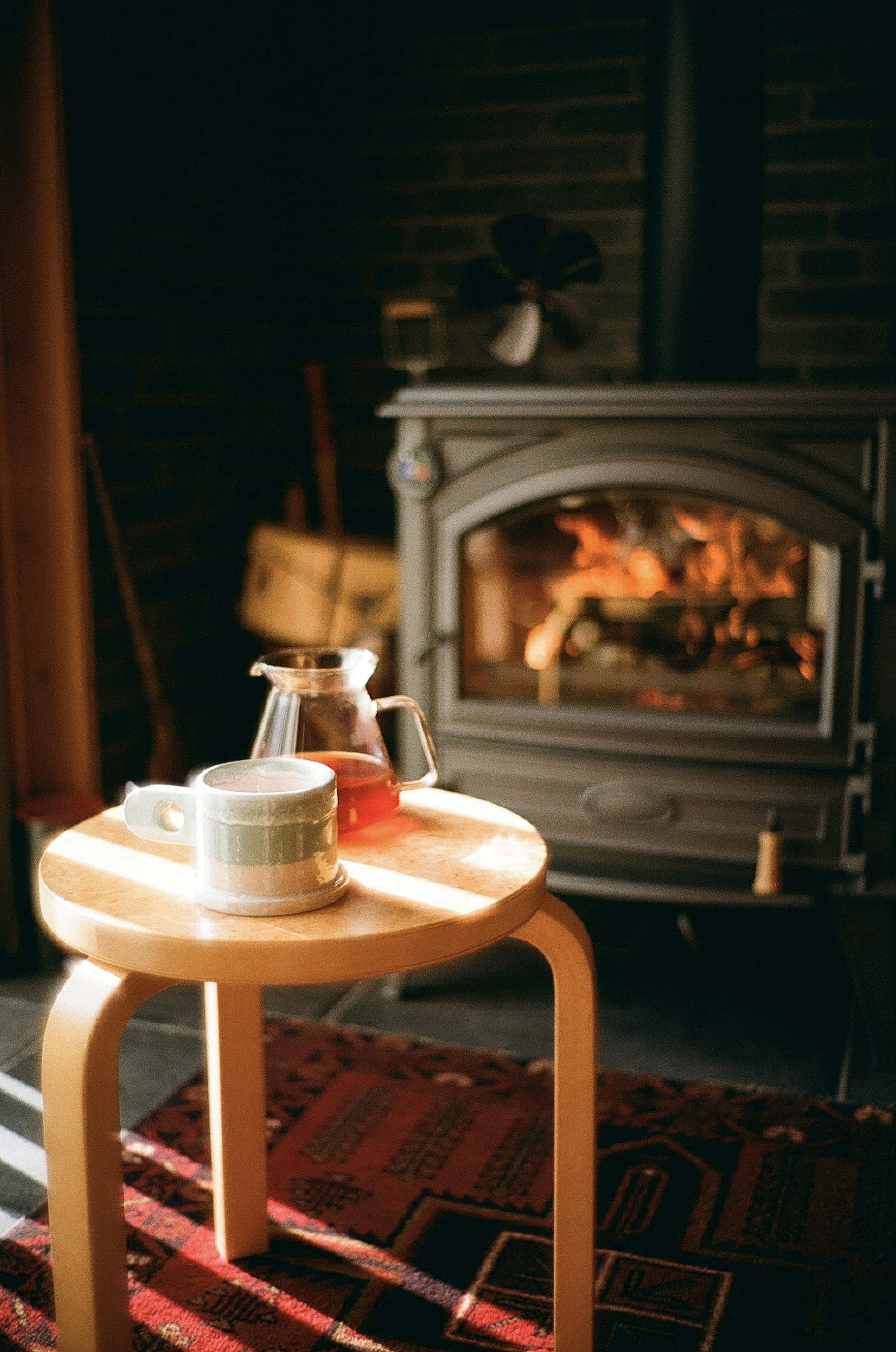 A simple wooden table with a tea set in front of a cozy fireplace