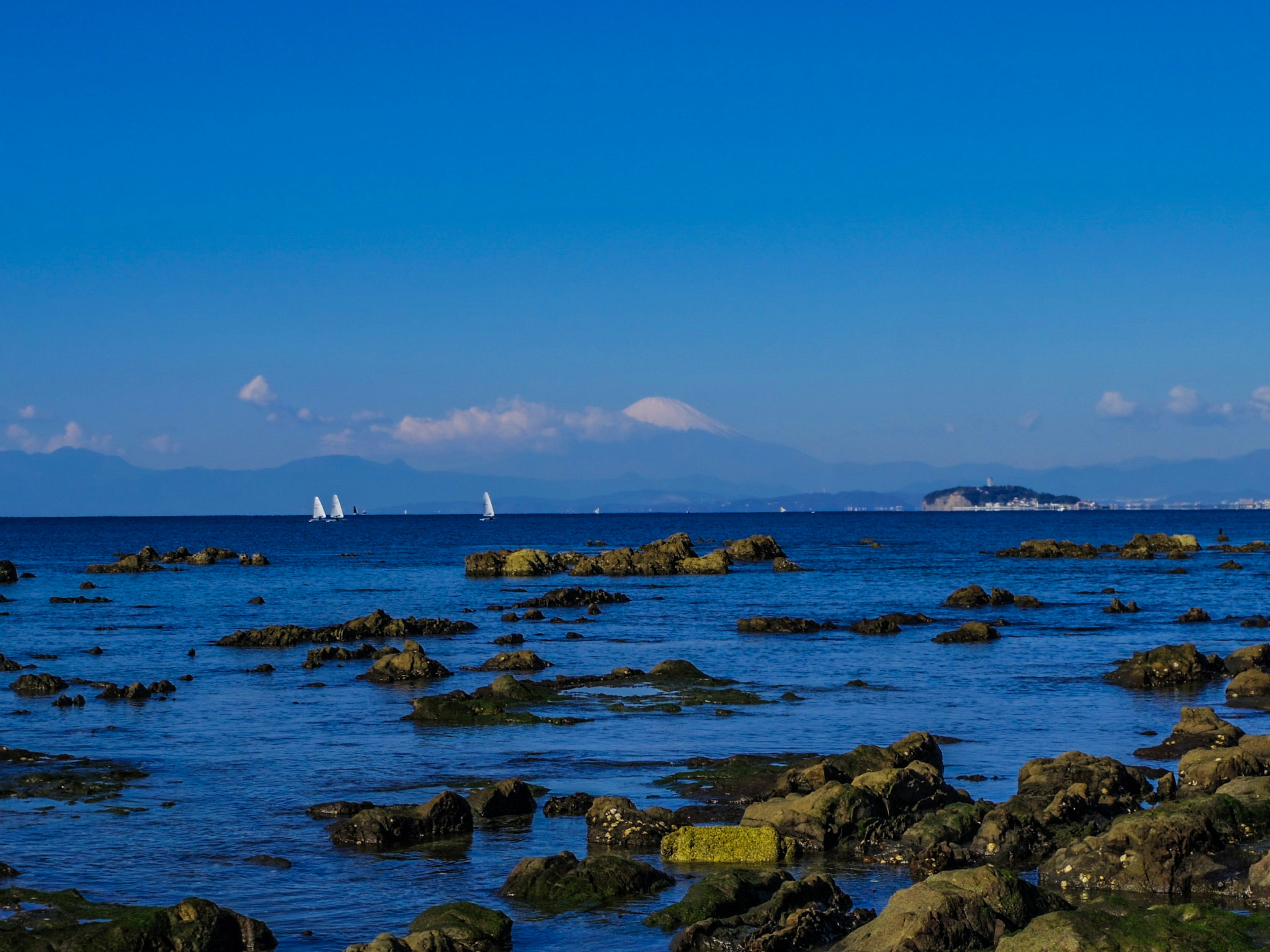 Vista panoramica dell'oceano blu con una costa rocciosa e velieri bianchi