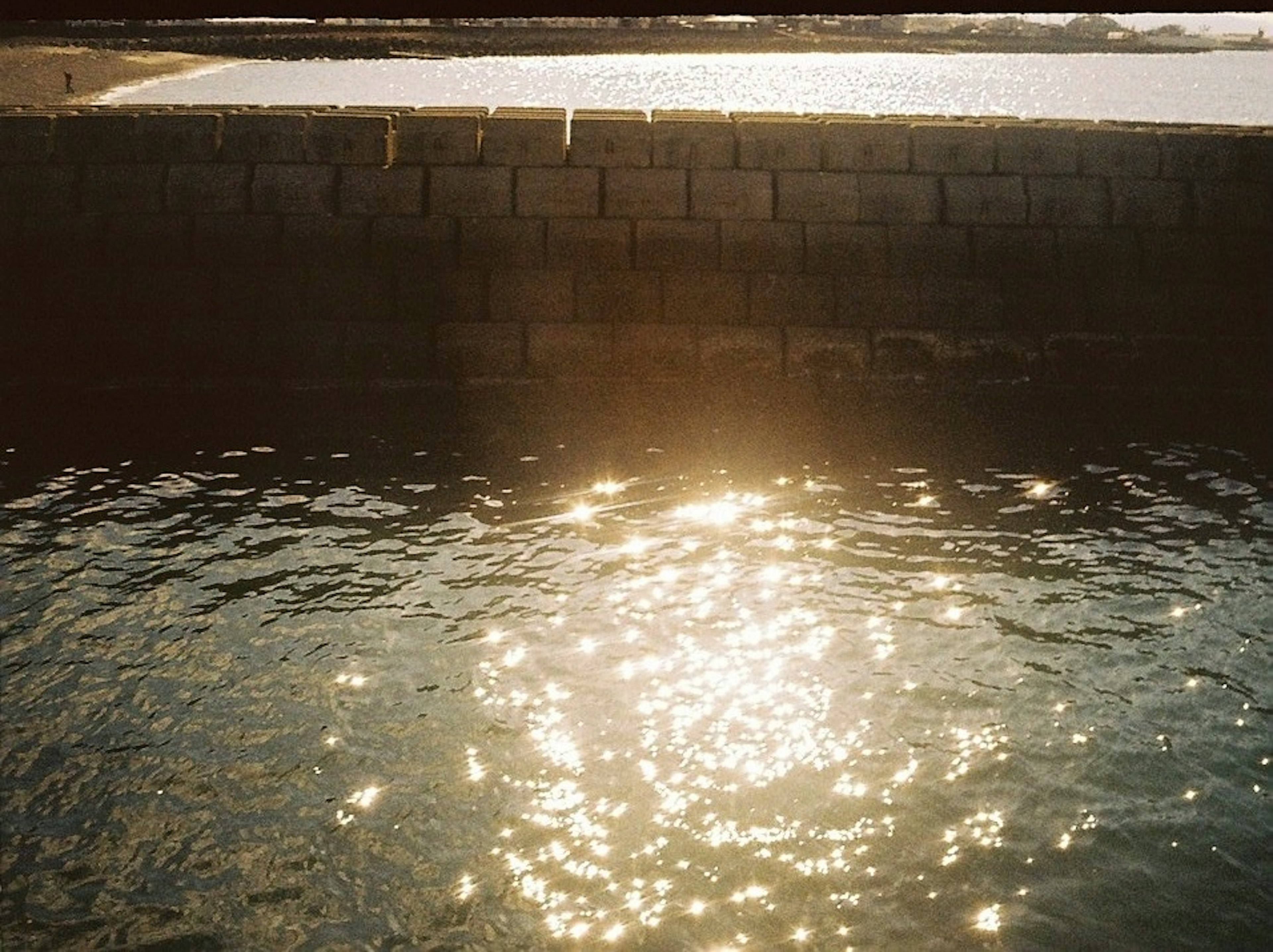 Sunlight reflecting on water surface with stone wall