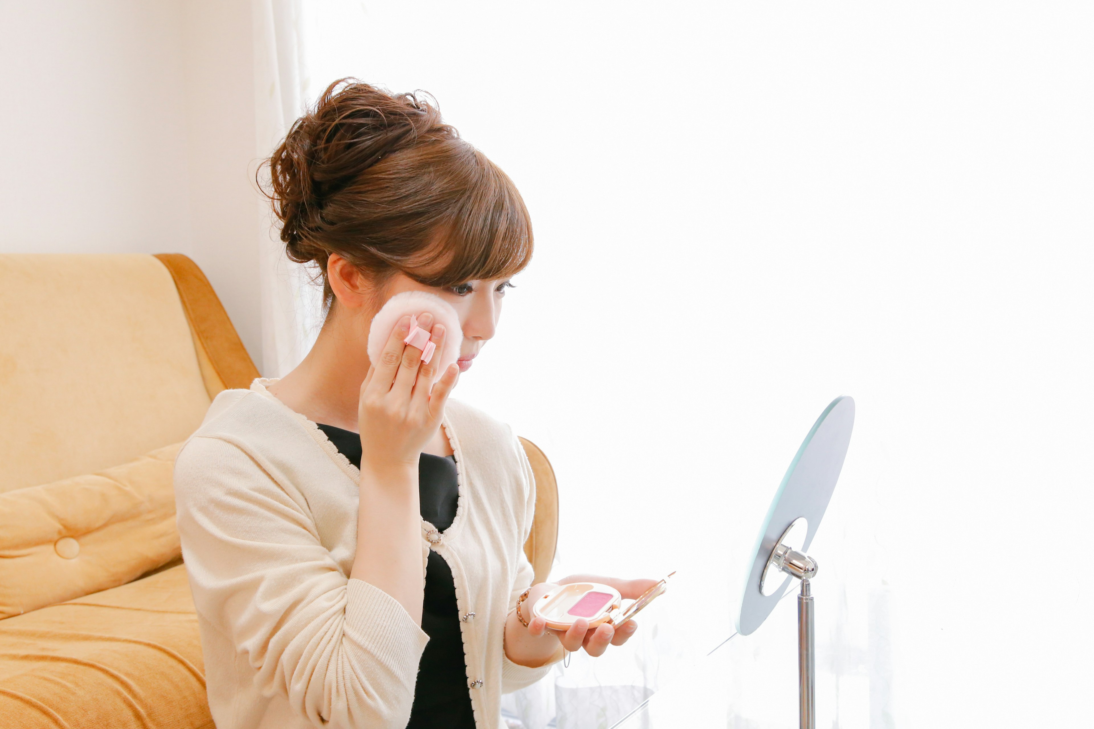 Woman applying makeup in front of a mirror indoors