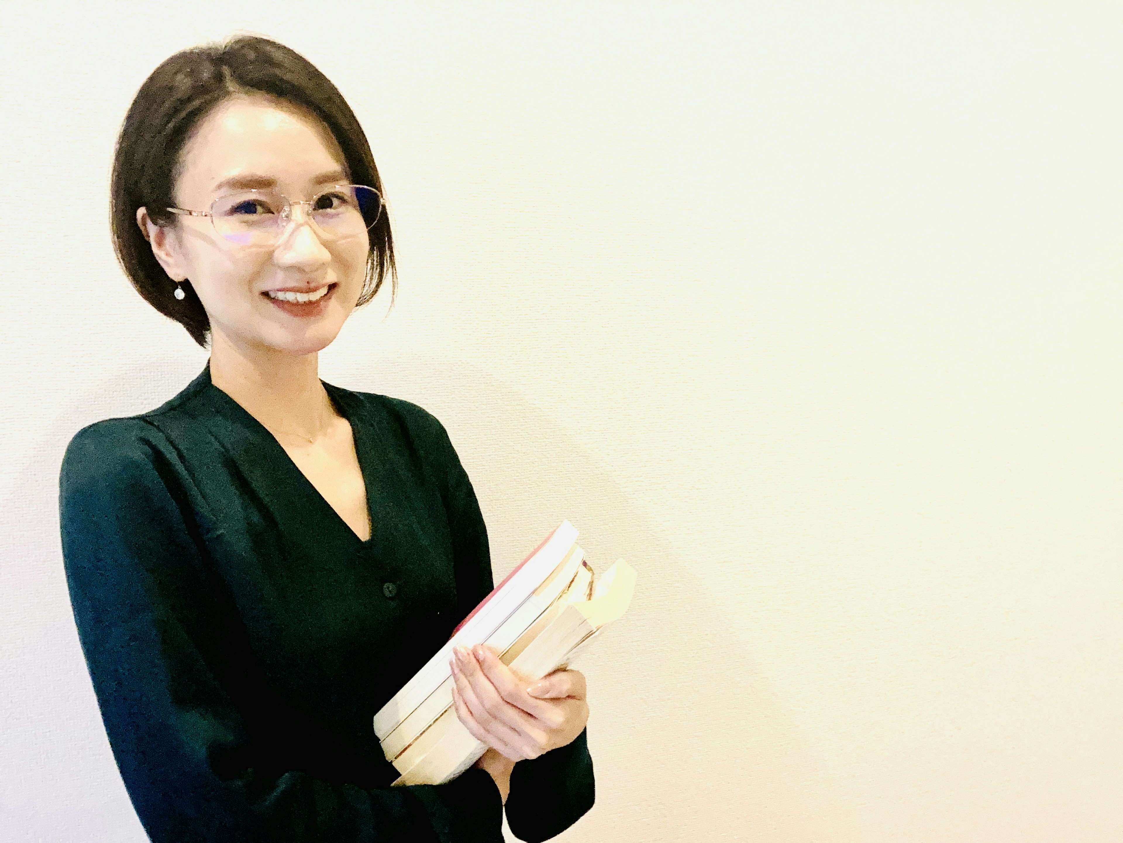 Una mujer sonriendo mientras sostiene libros frente a un fondo simple