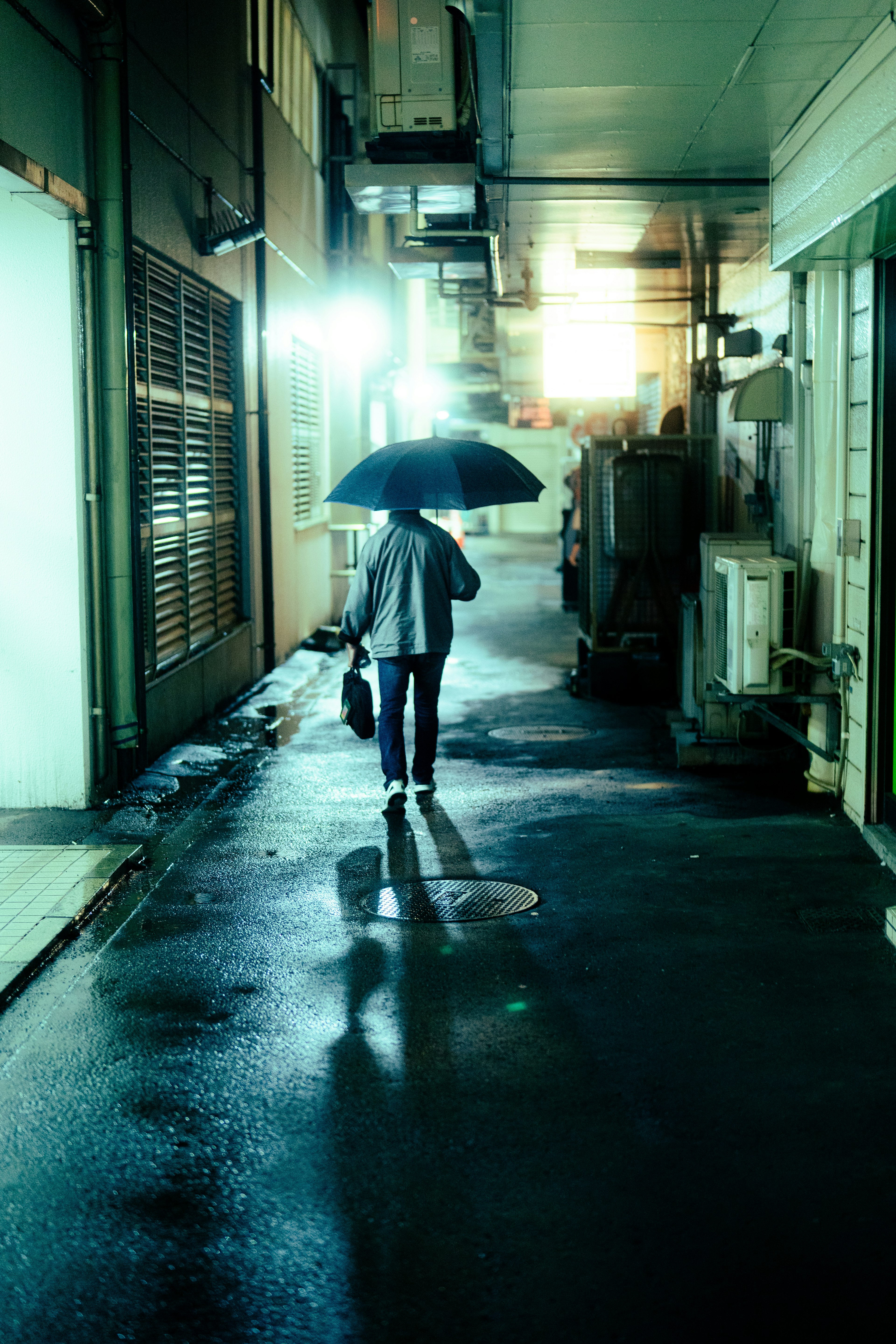 Person walking with an umbrella in a dimly lit alley during rain