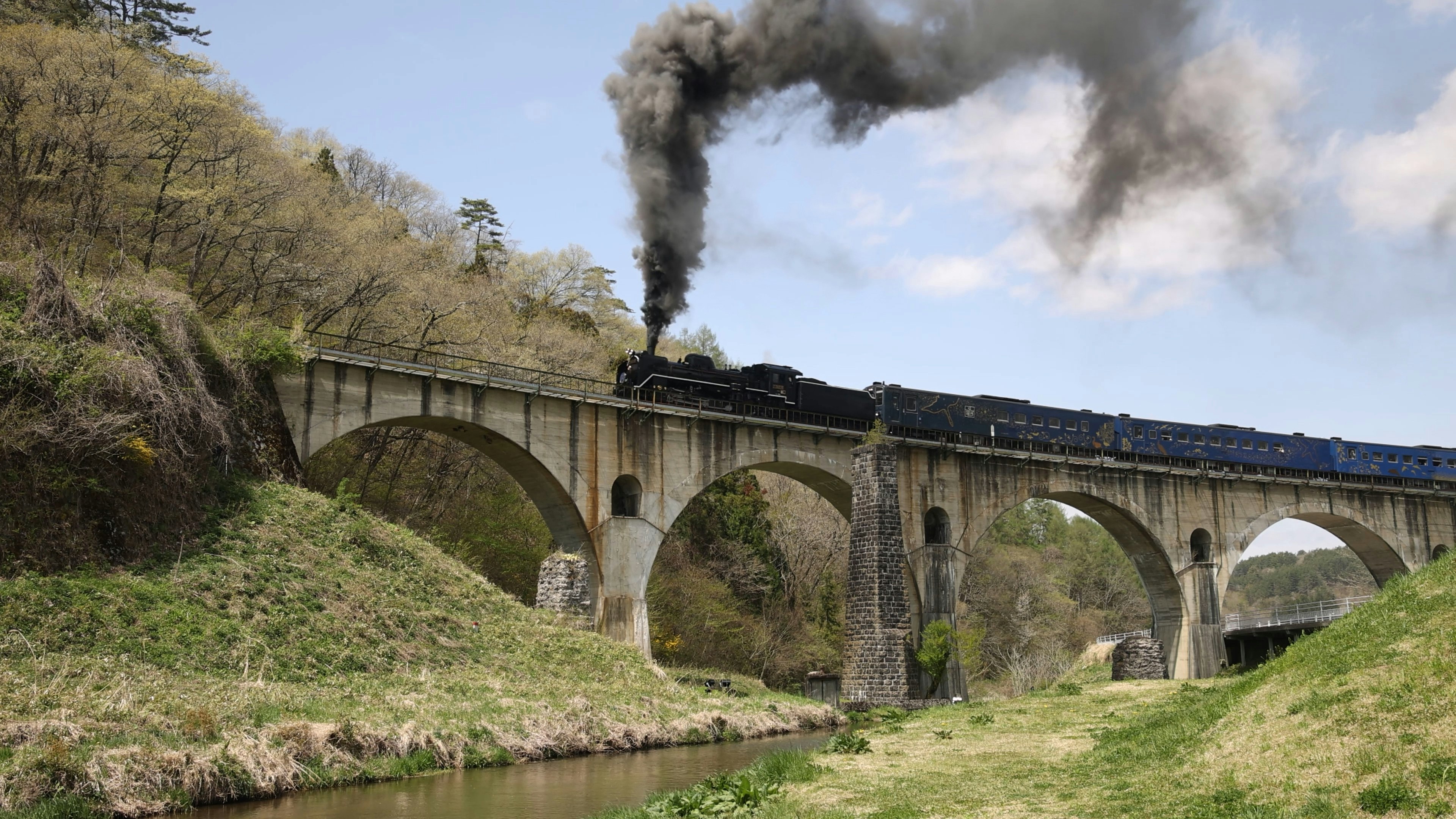 Steam locomotive emitting smoke crossing a scenic bridge