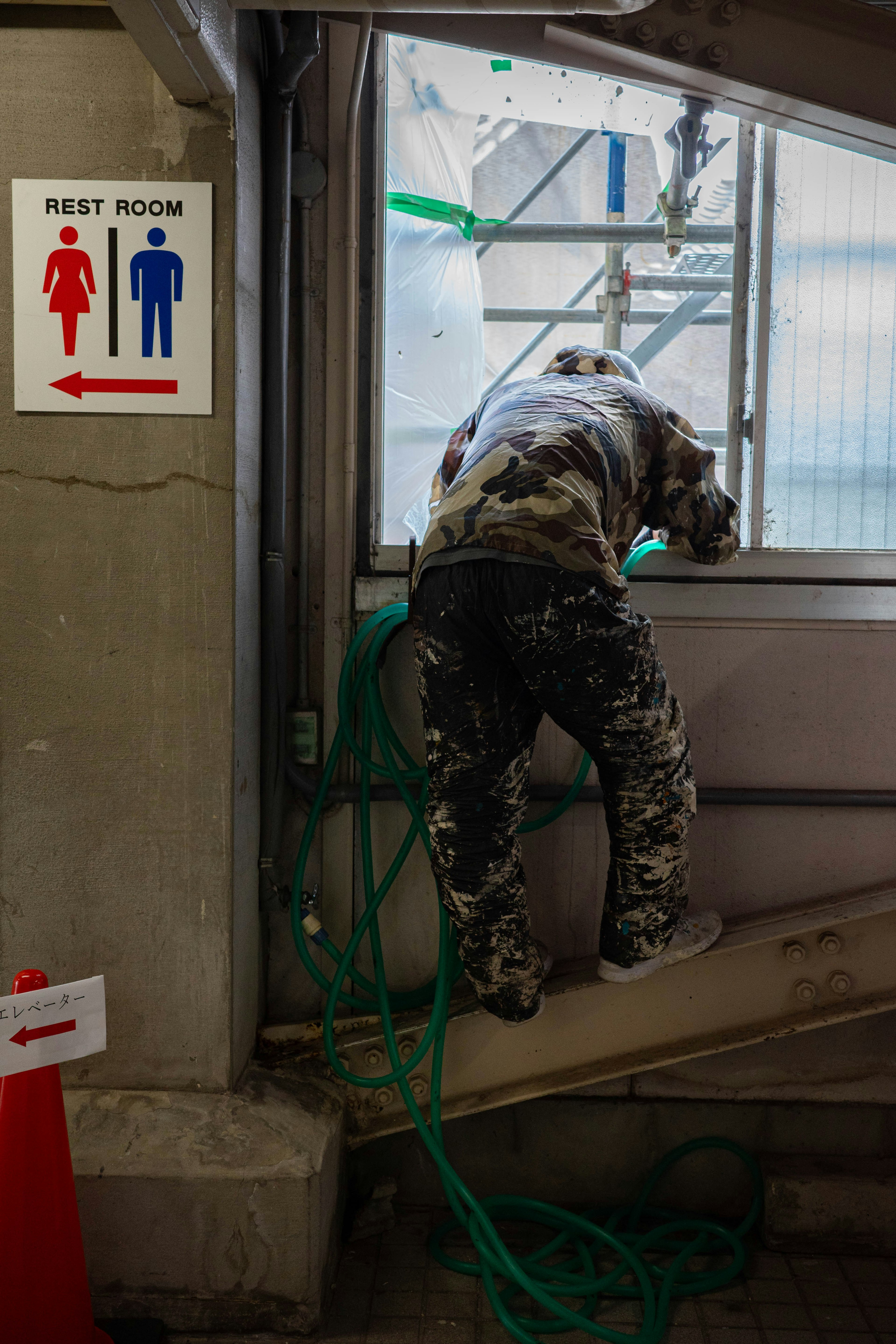 Ein Arbeiter auf einer Baustelle, der aus einem Fenster schaut, mit einem nahegelegenen Toilettenschild