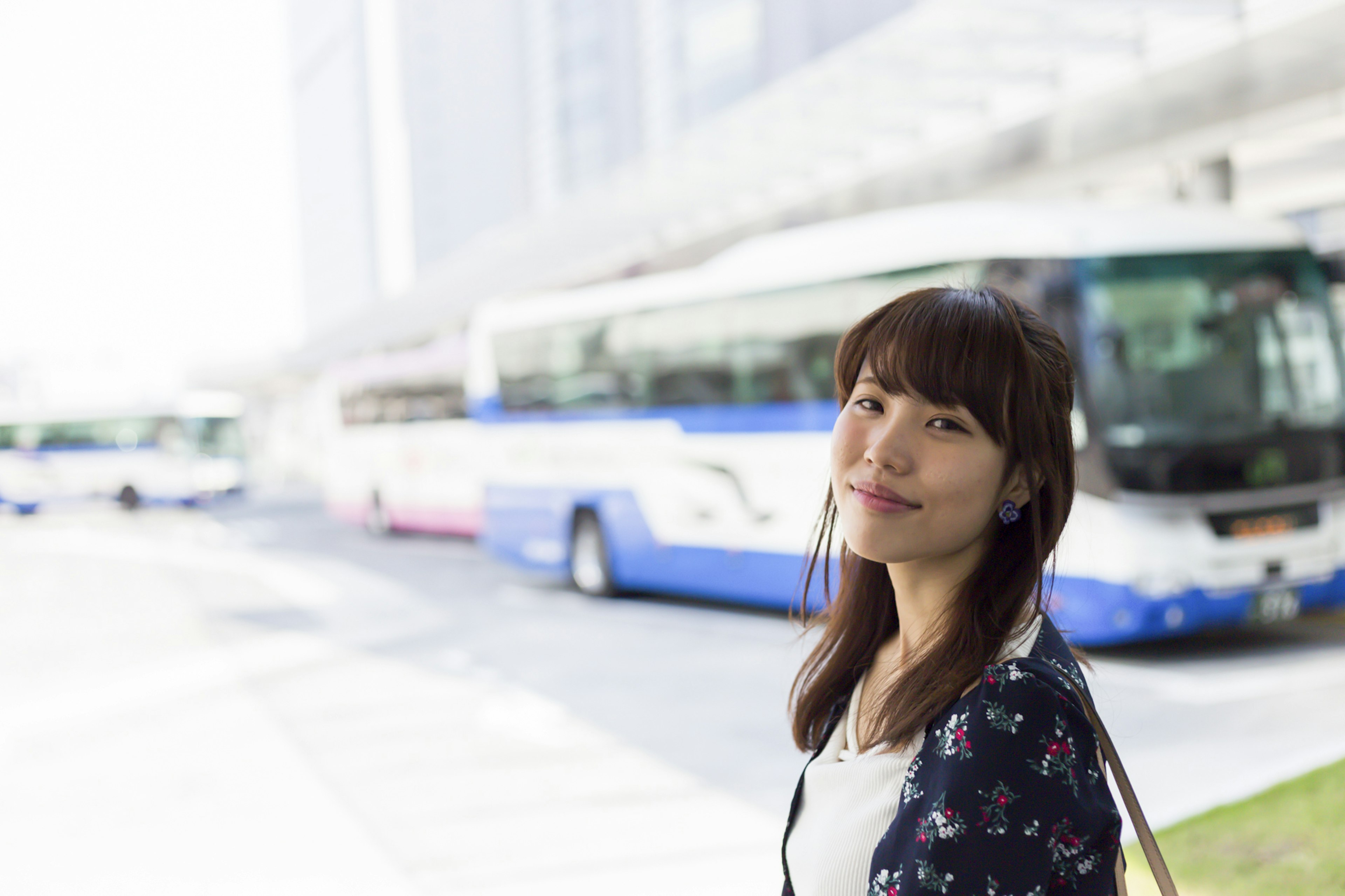 Une femme souriante à un arrêt de bus avec des bus en arrière-plan