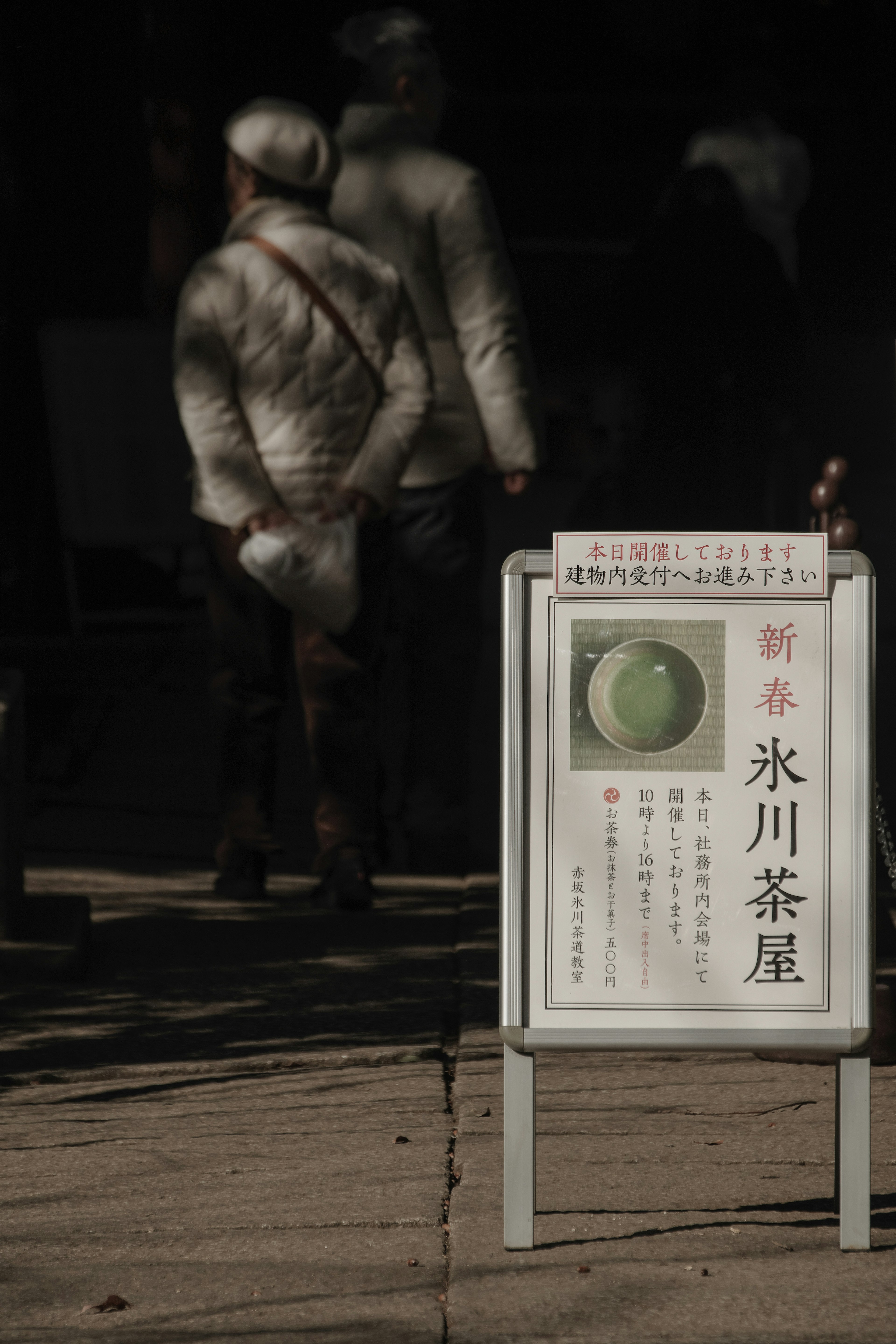 Cartel del nuevo Hikawa Teahouse con personas caminando al fondo