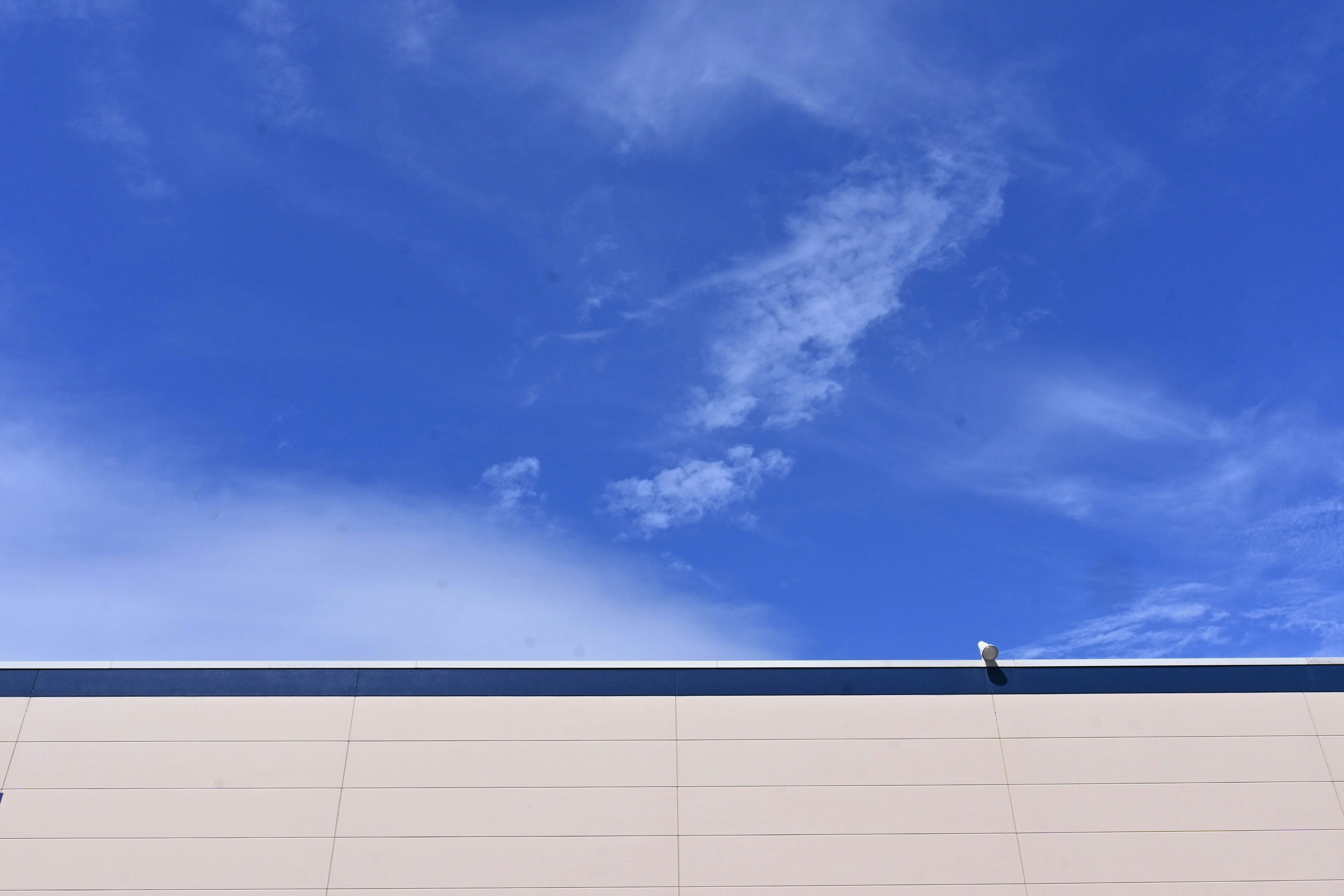 Building wall against a clear blue sky with wispy clouds