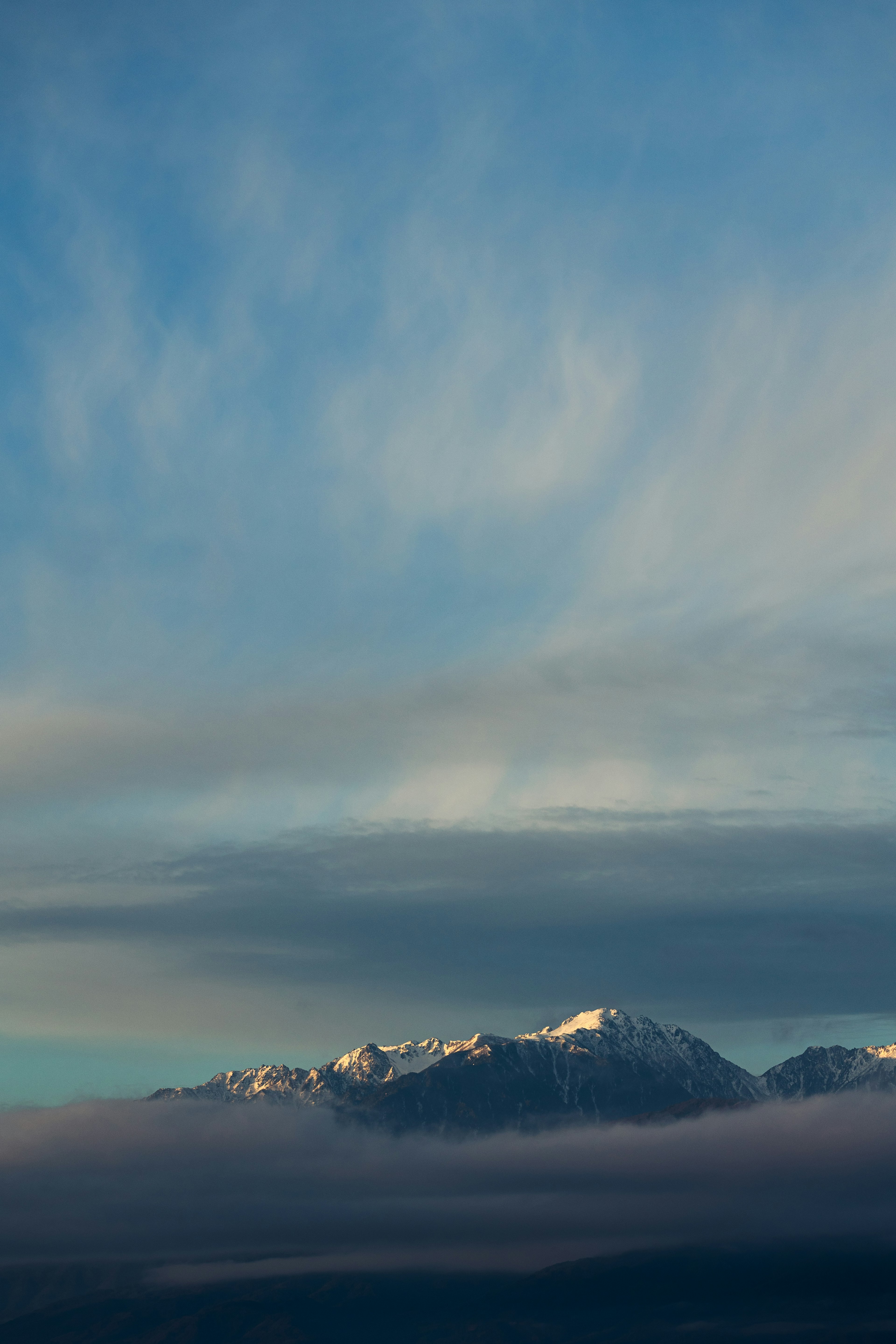 Snow-capped mountains under a blue sky with wispy clouds