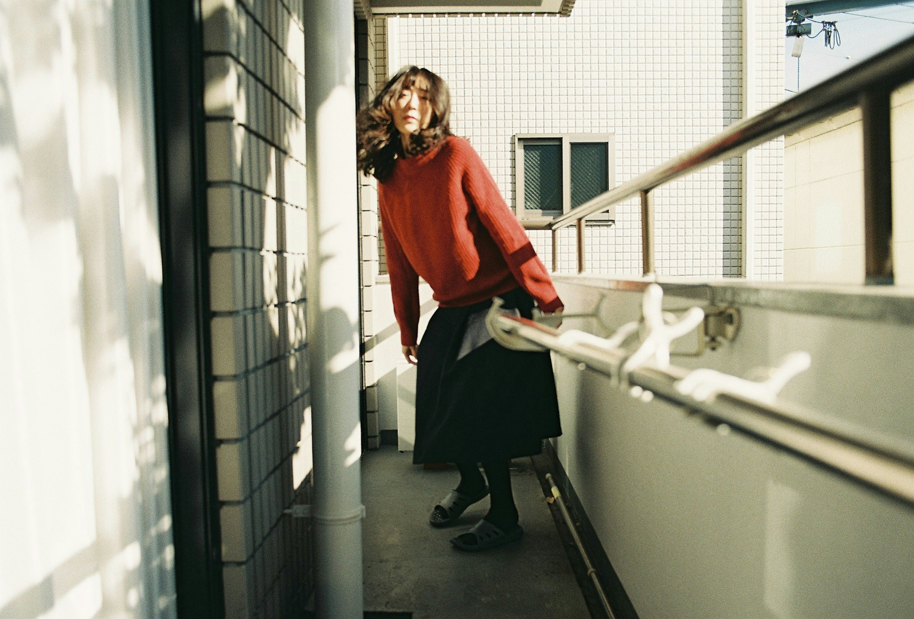 Una donna in maglione rosso e gonna nera che posa su un balcone