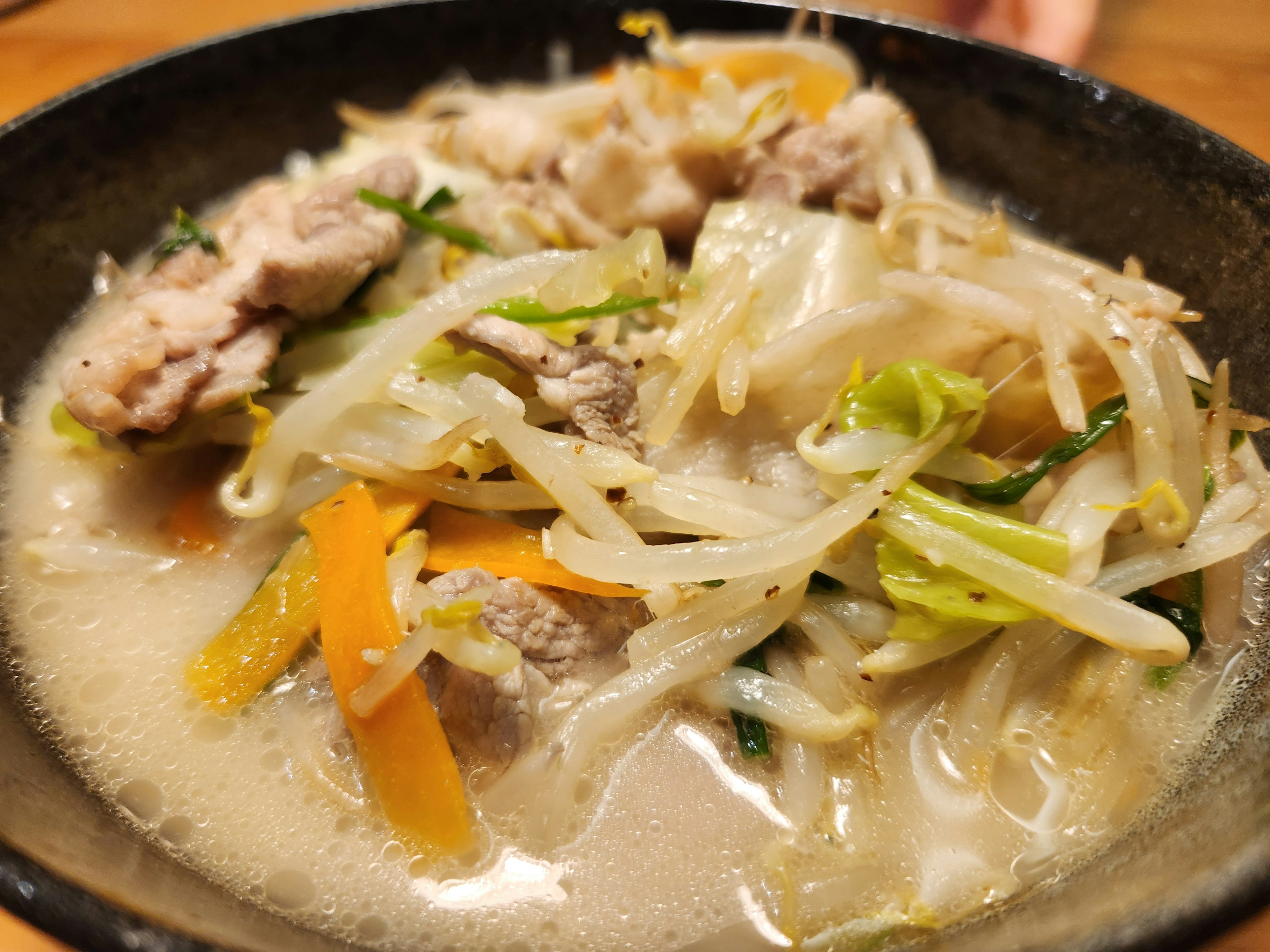 A bowl of rich soup with assorted vegetables and pork