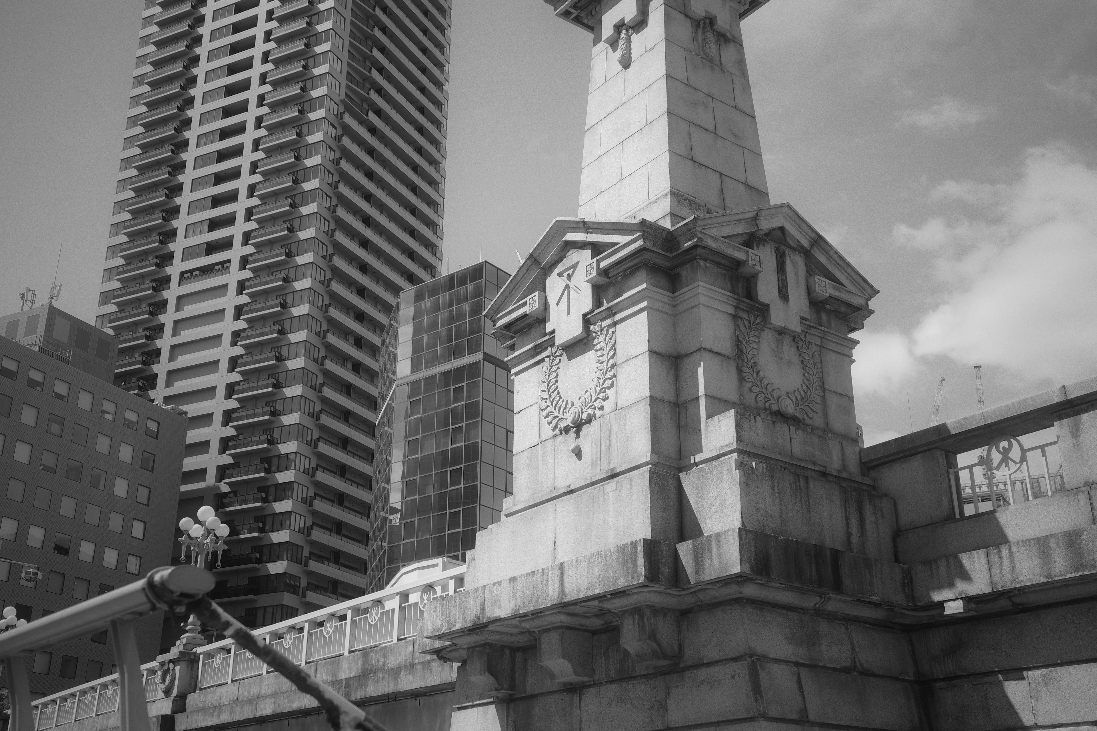 Foto monokrom dari monumen tua dengan gedung pencakar langit di latar belakang