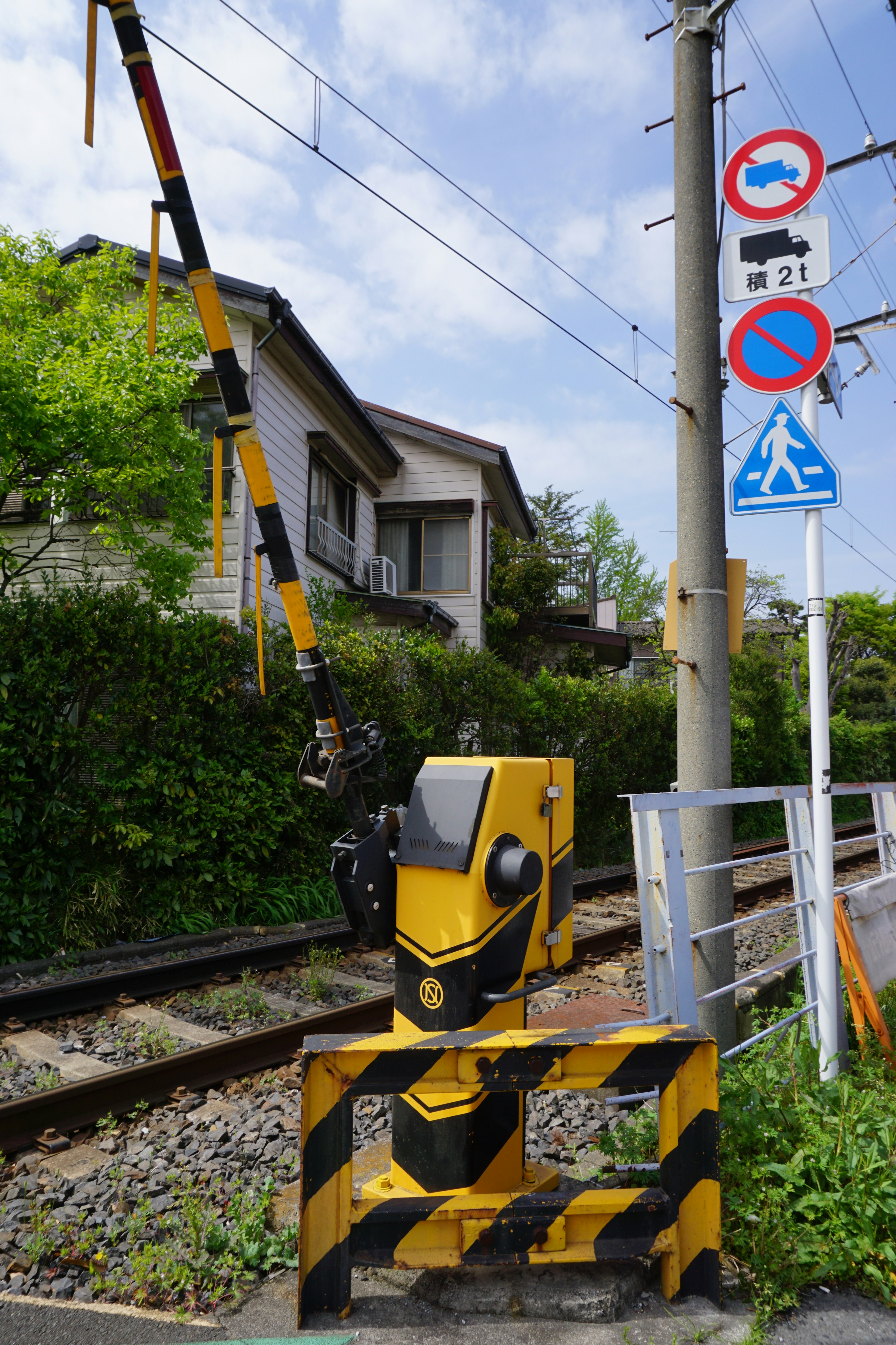 Un segnale giallo e un cartello di avvertimento vicino ai binari con una casa sullo sfondo