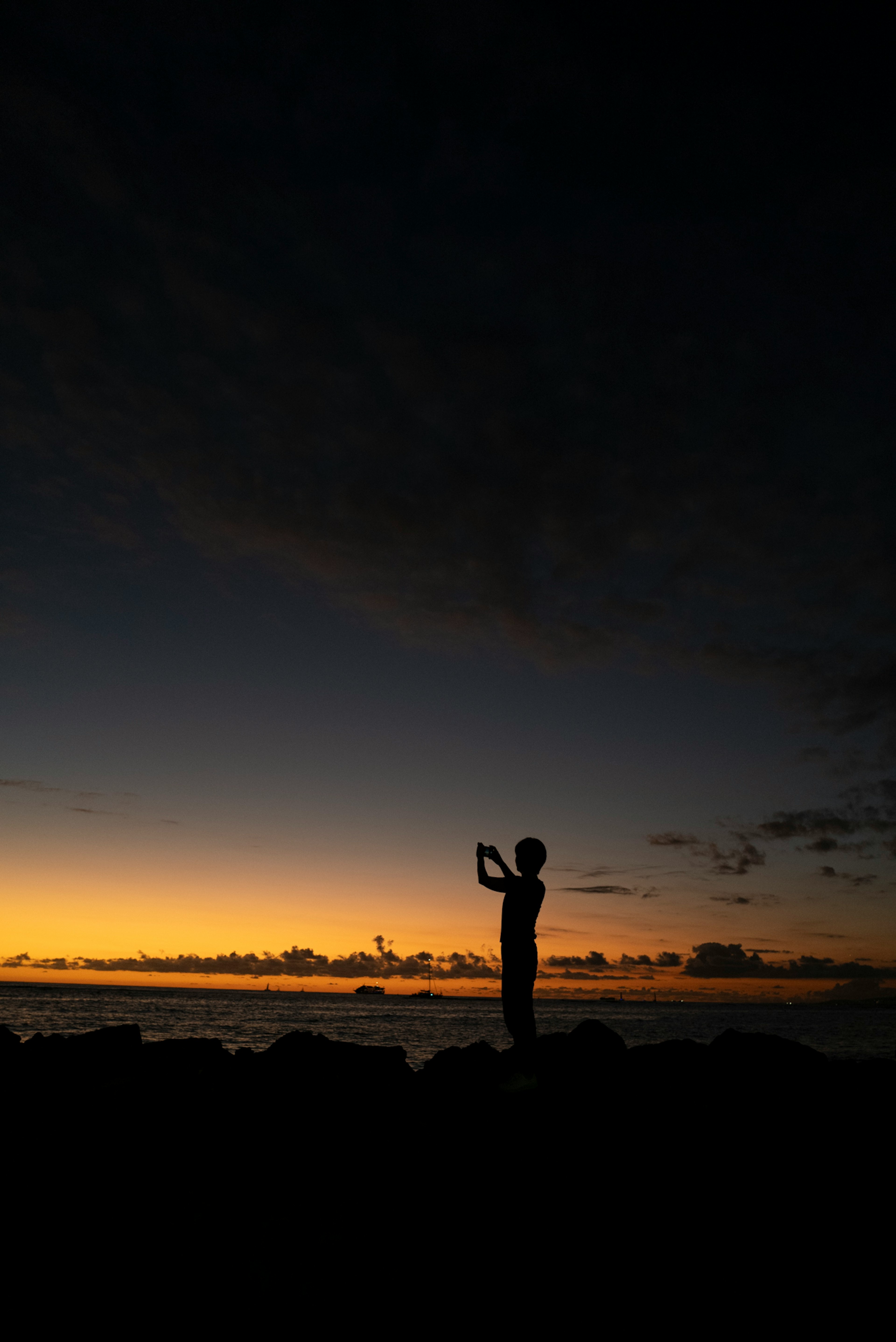 Silhouette einer Person, die bei Dämmerung am Meer ein Smartphone hält