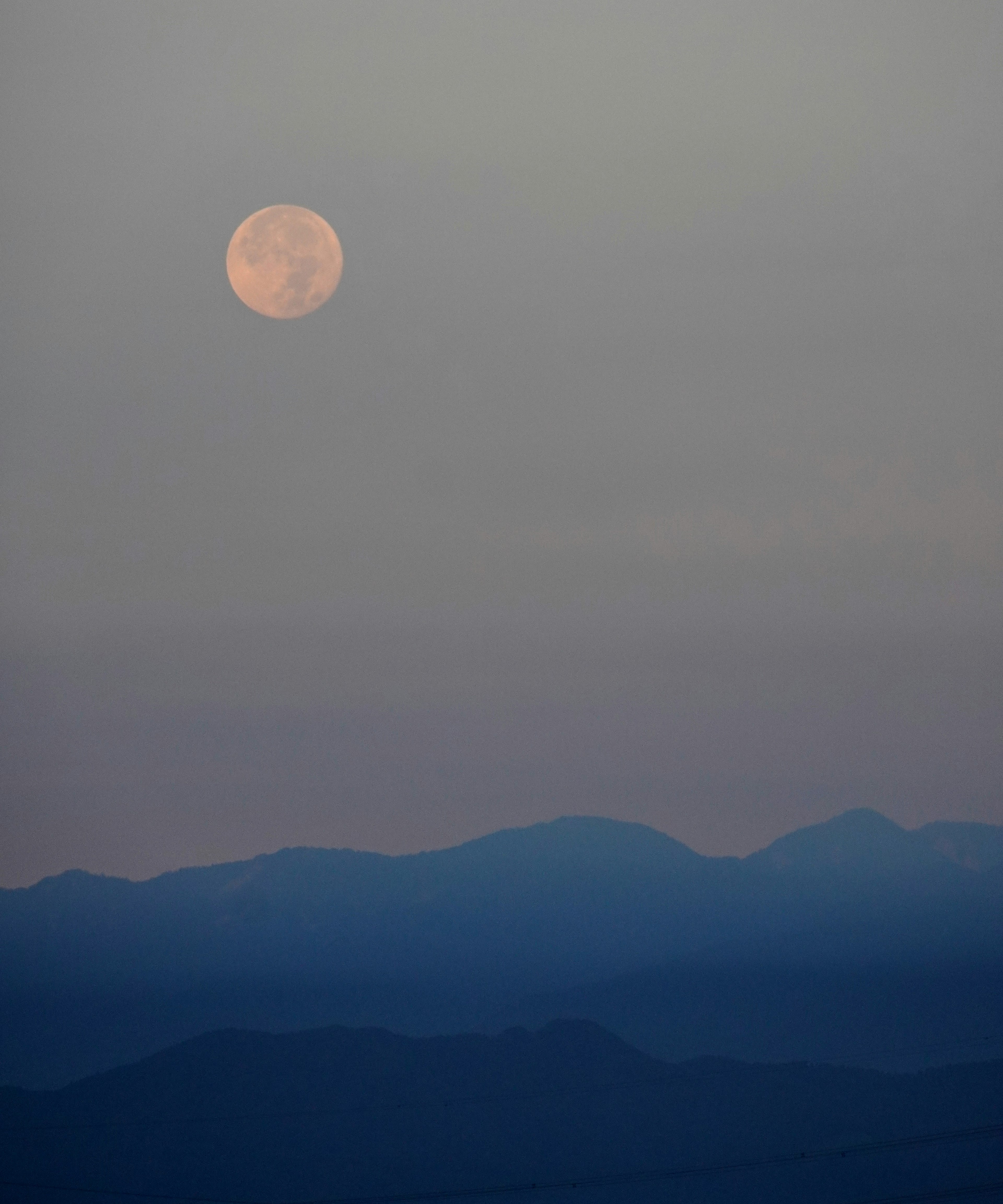 Bulan purnama terbit di atas pegunungan jauh saat senja