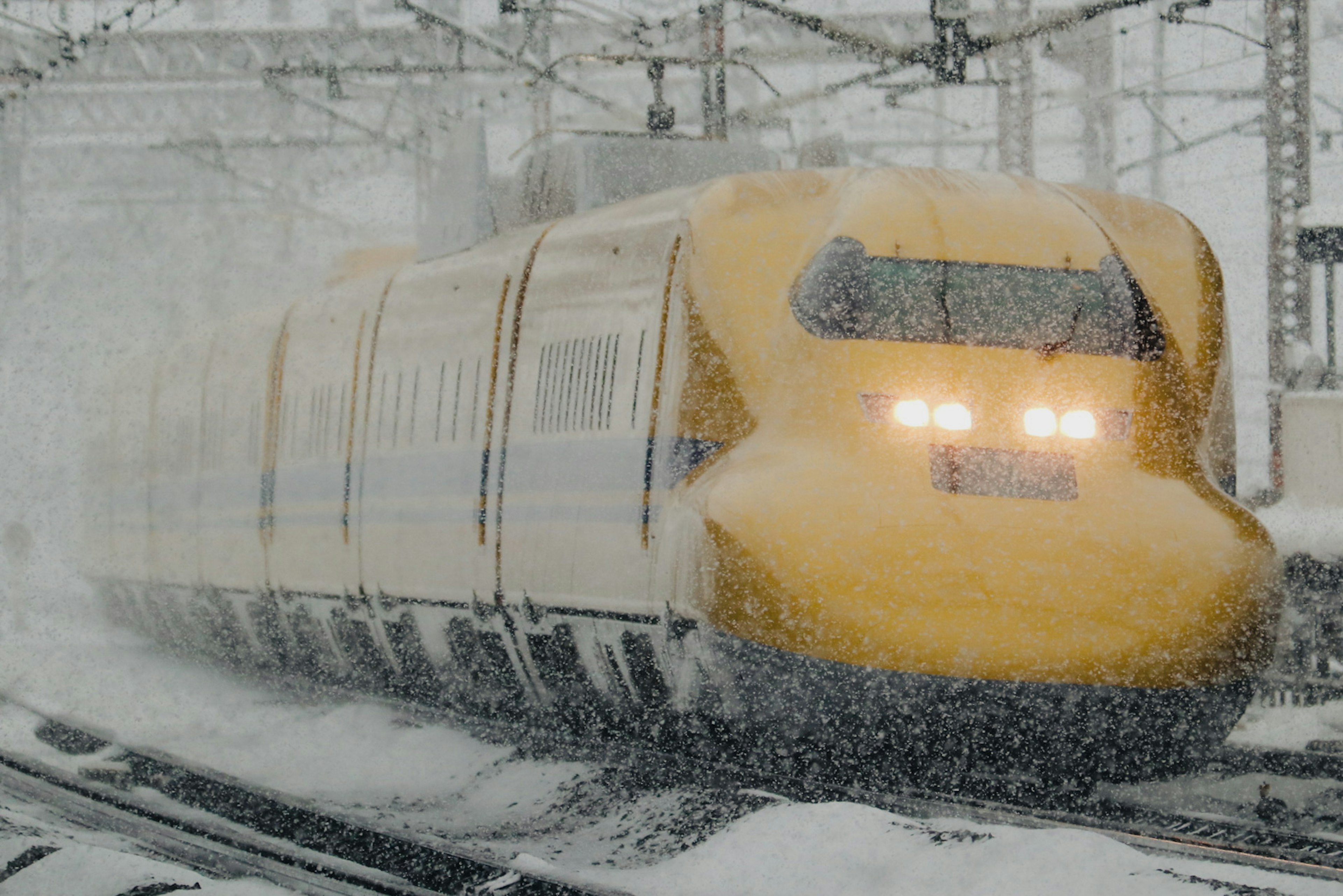 雪の中を走る黄色い新幹線の画像