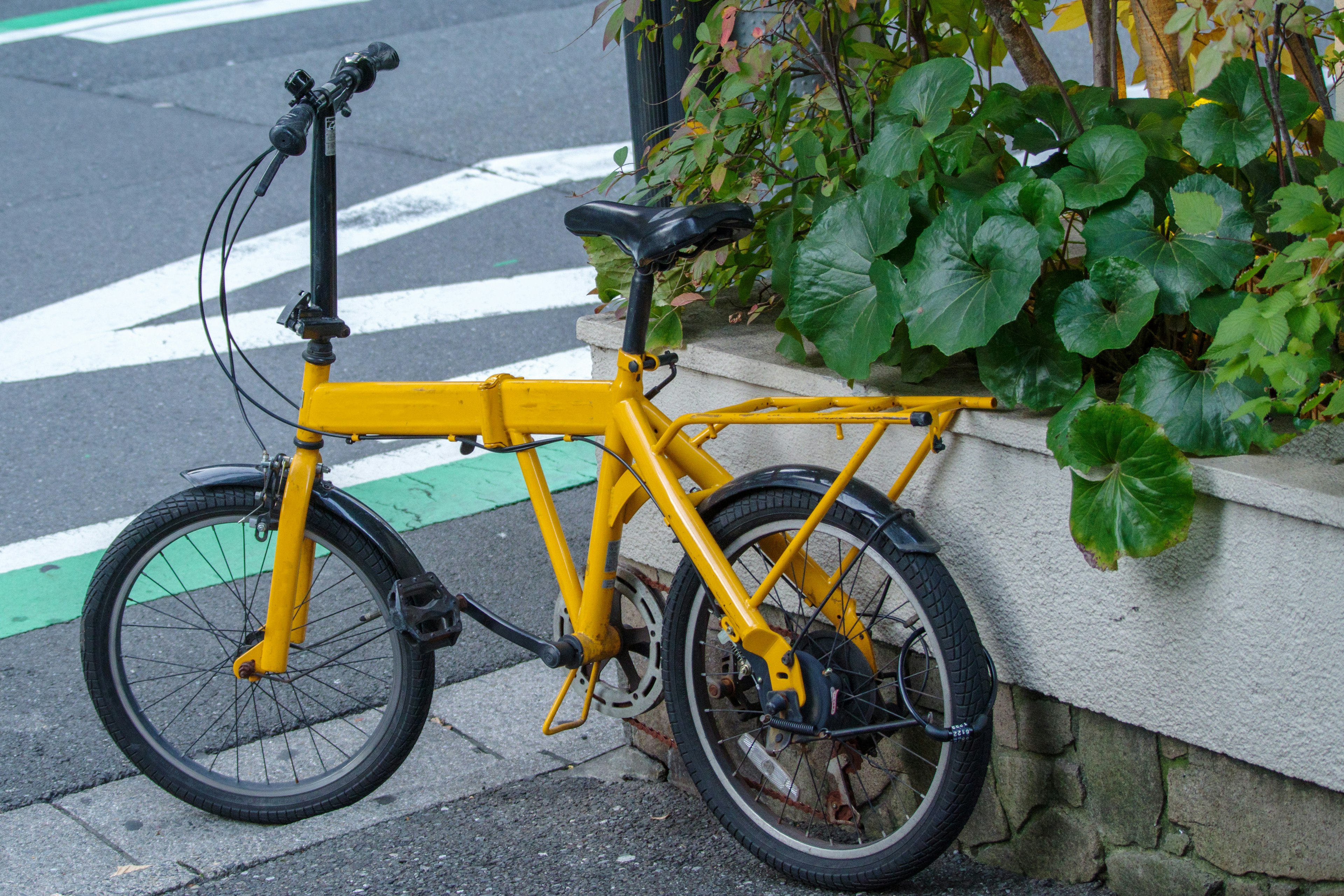 A yellow folding bicycle leaning against a wall near greenery