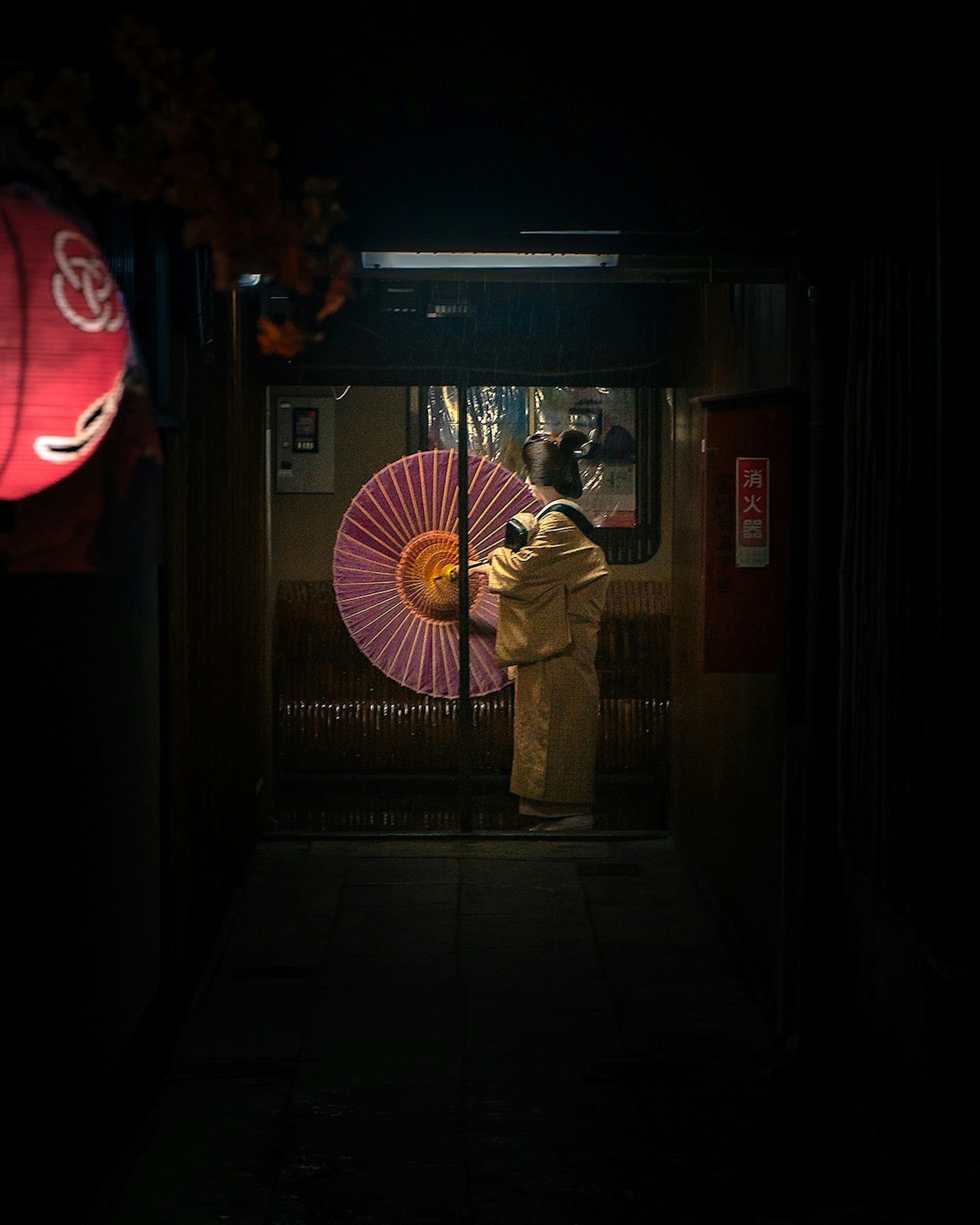 Eine Frau im Kimono hält einen traditionellen Regenschirm in einer schwach beleuchteten Gasse