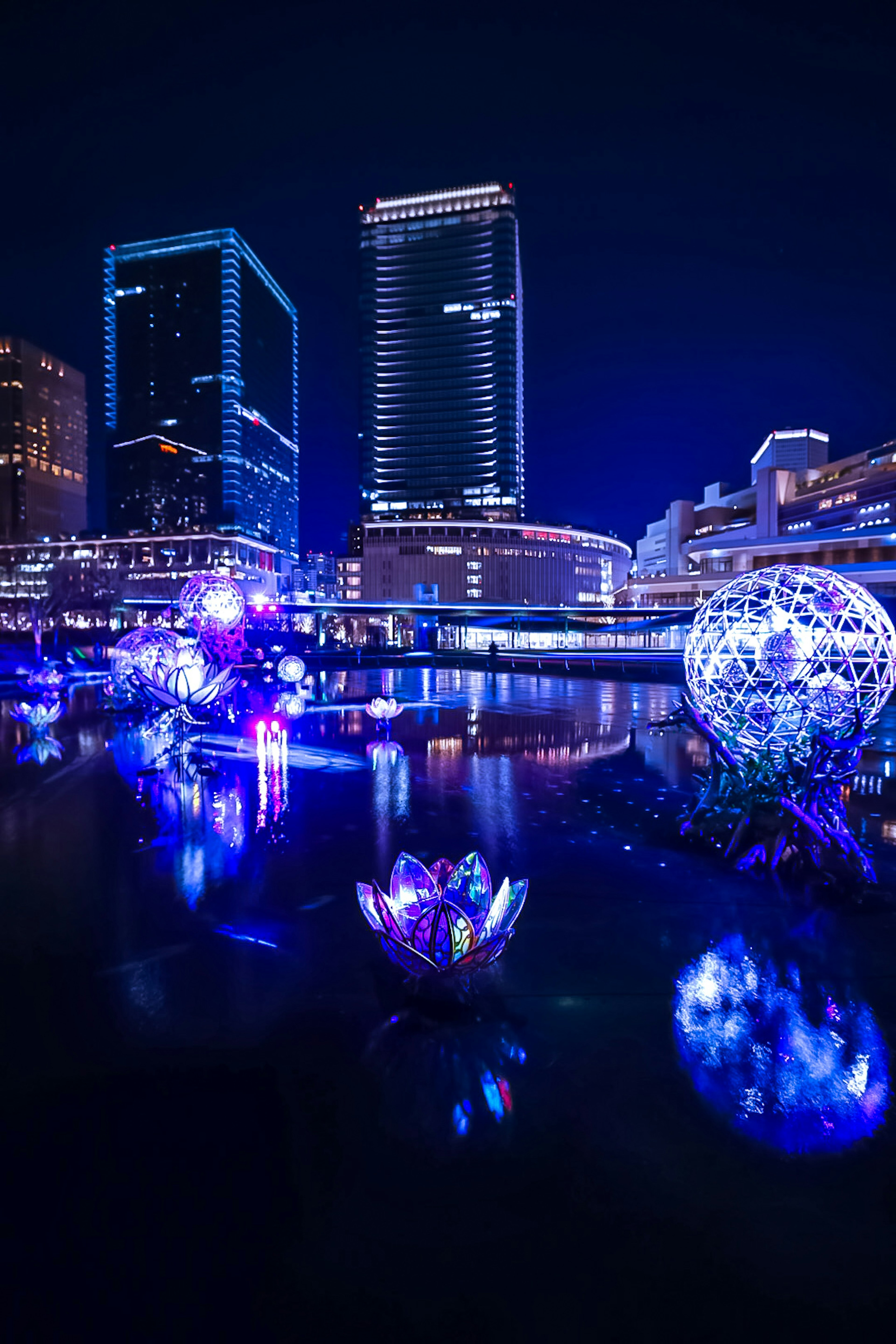 夜の都市のライトアップされたビルと水面に浮かぶ幻想的な花のオブジェ