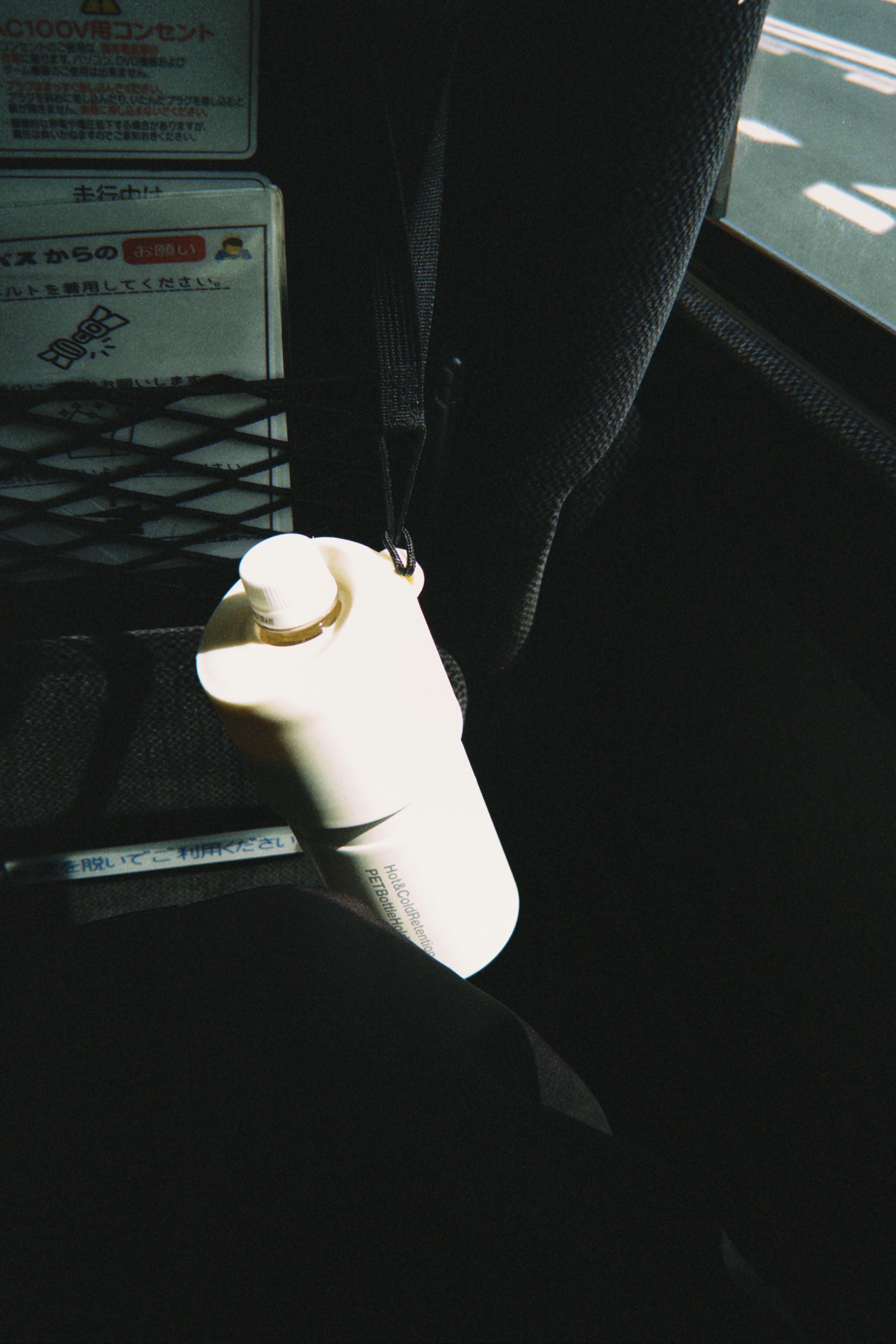 A white bottle hanging on a bus seat with a dark fabric background