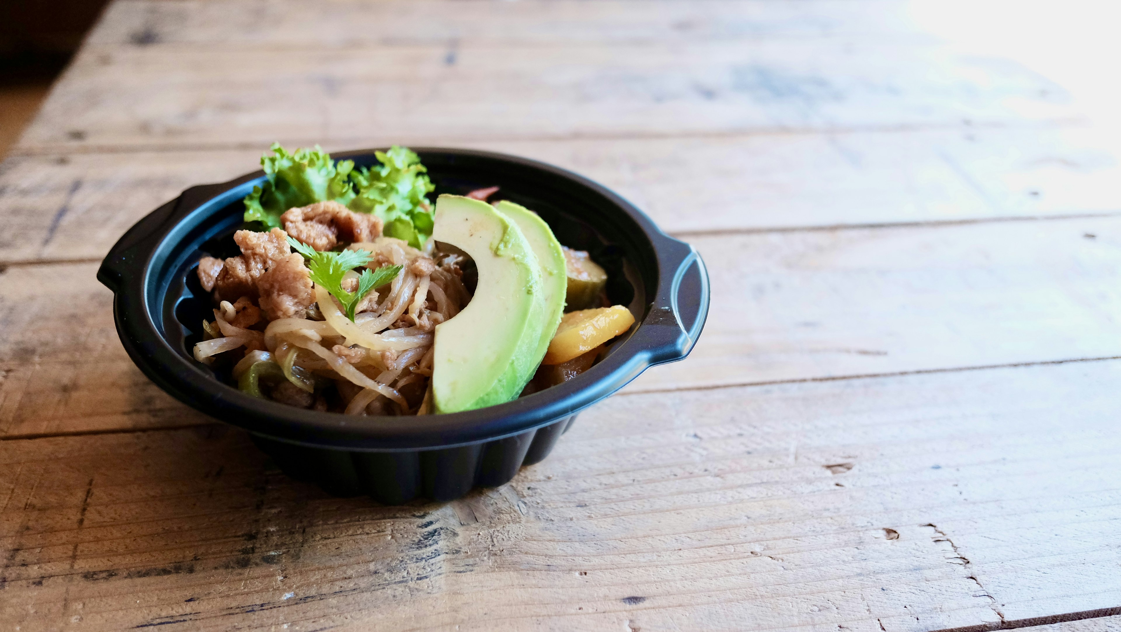 Gericht in einer schwarzen Schüssel mit Avocadoscheiben und grünem Gemüse